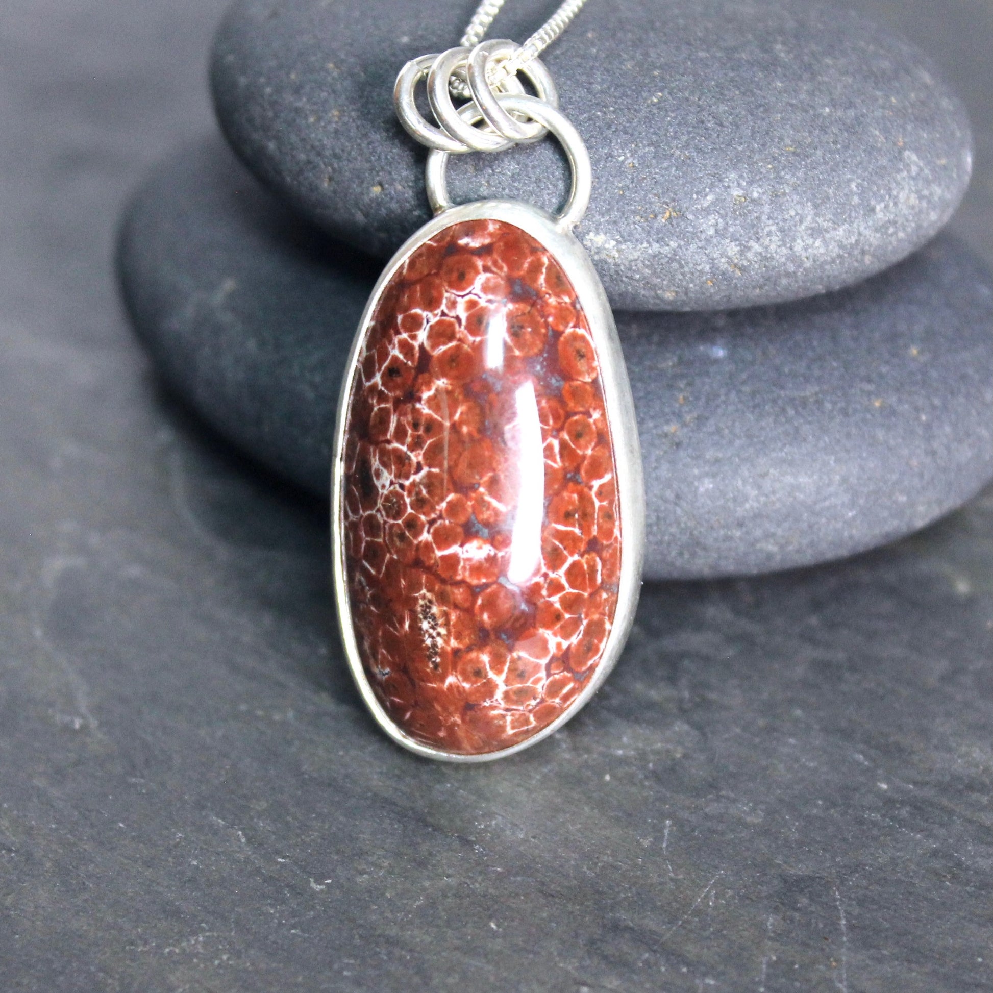 May include: A silver chain necklace with a red and white oval pendant. The pendant is made of a natural stone with a unique pattern.