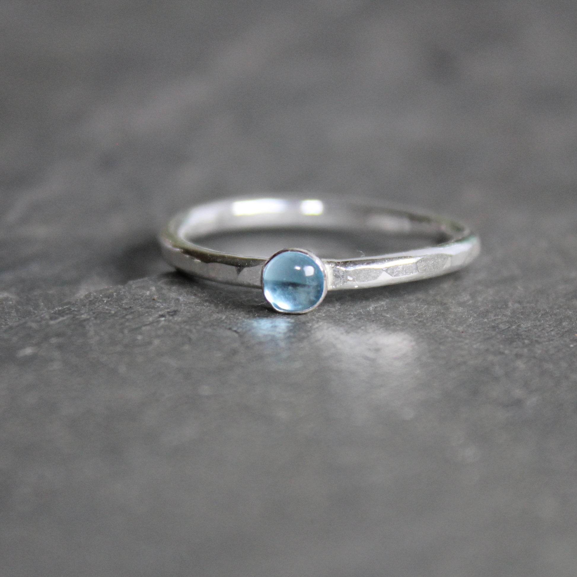 A 4mm round blue topaz cabochon set in a handmade sterling silver bezel setting on a sturdy silver band. 