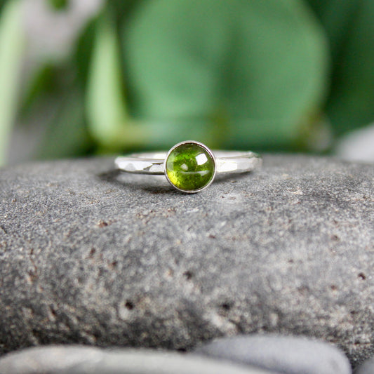 A Round 6mm green tourmaline gemstone set in a sterling silver bezel setting on a sturdy hammered band. 