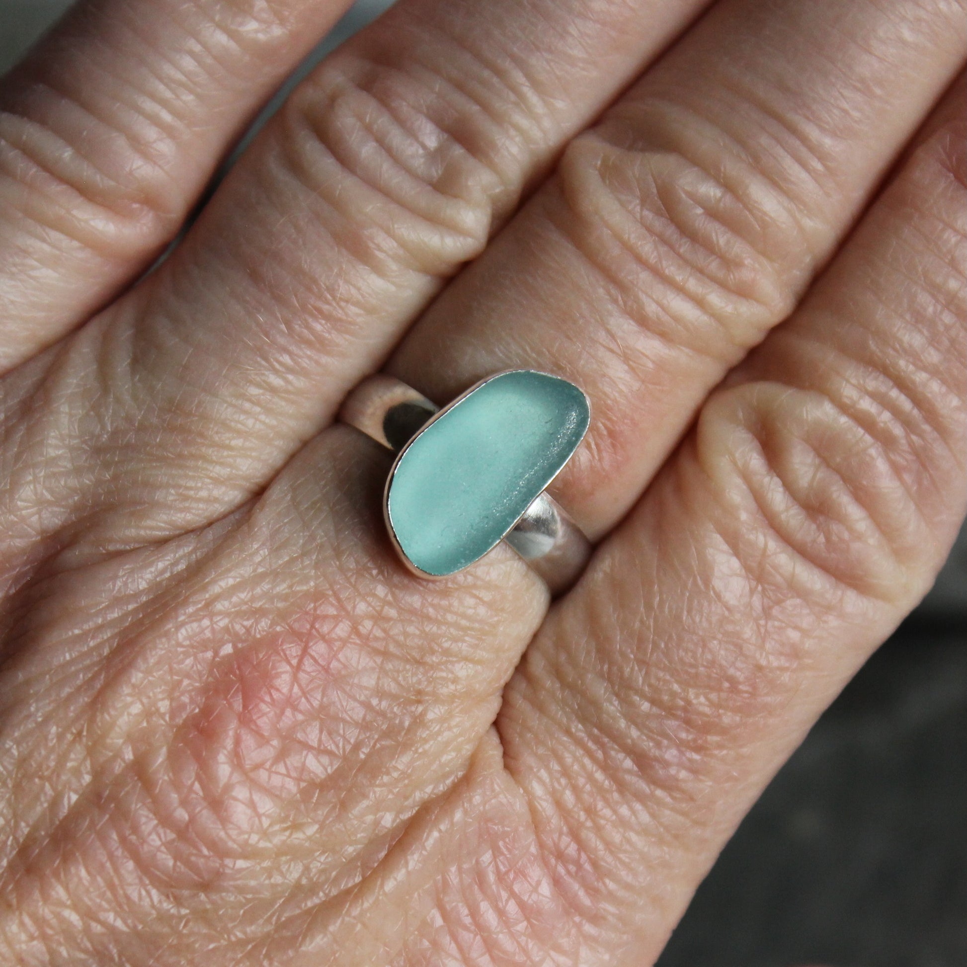 An oblong piece of aqua blue sea glass set in a fine and sterling silver bezel setting on a sturdy silver band. 