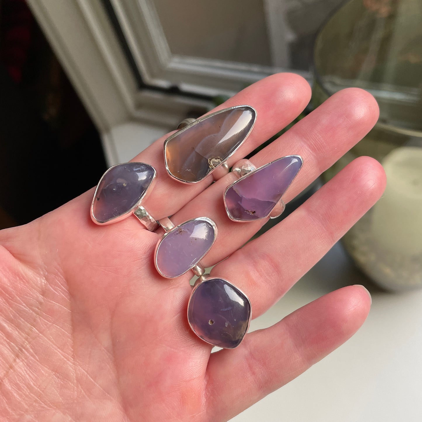 A hand showing a collection of 5 handmade sterling silver Oregon Holley Blue agate statement rings. 