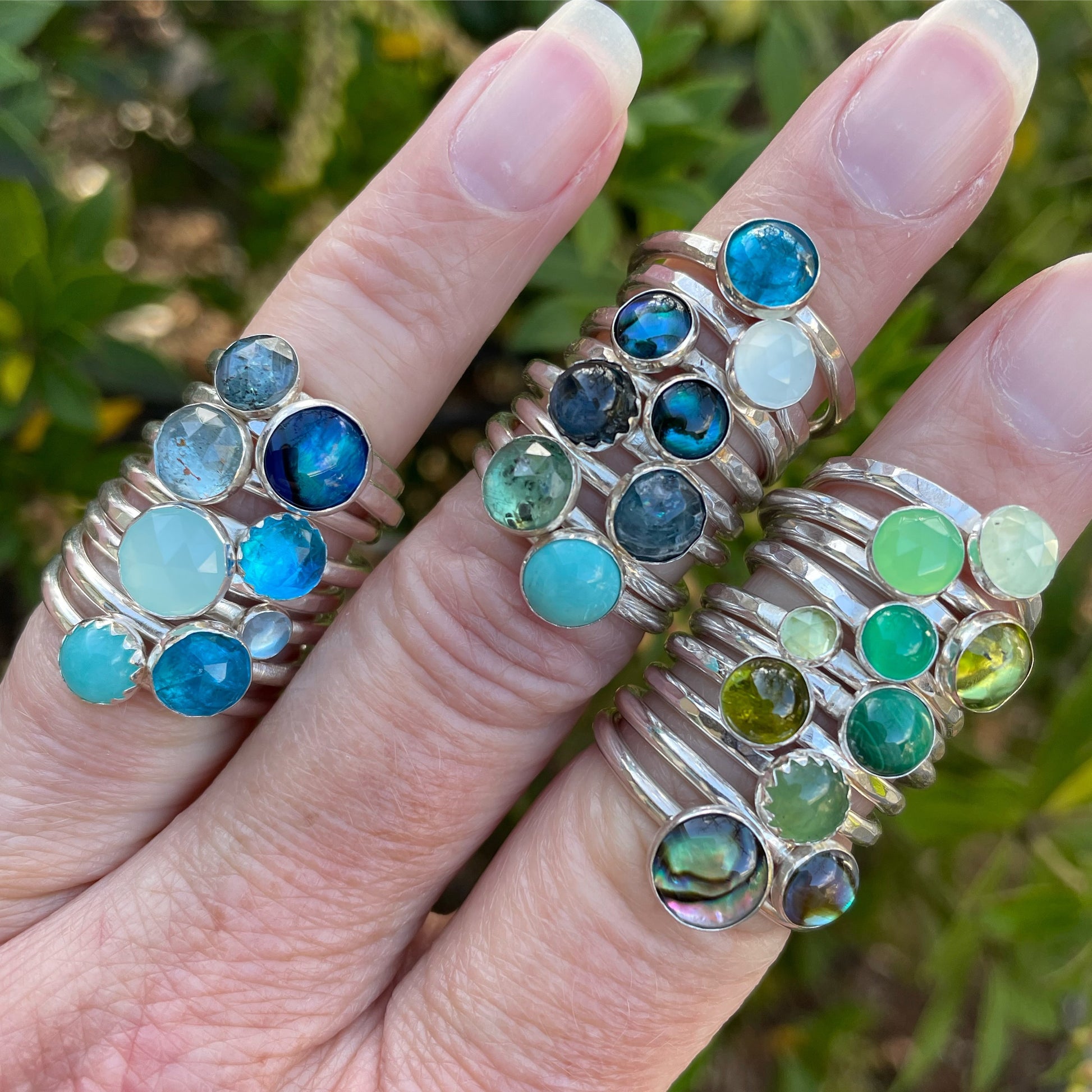 A collection of handmade blue and green gemstone stacking rings modeled on several fingers. 
