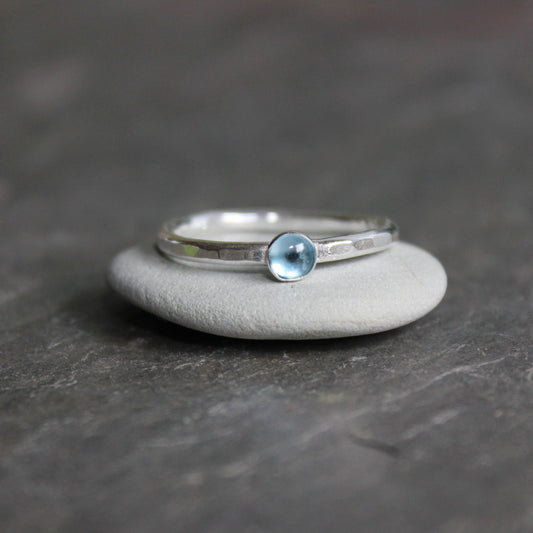 A tiny 4mm round blue topaz cabochon set in a sterling silver bezel on a sturdy silver band.