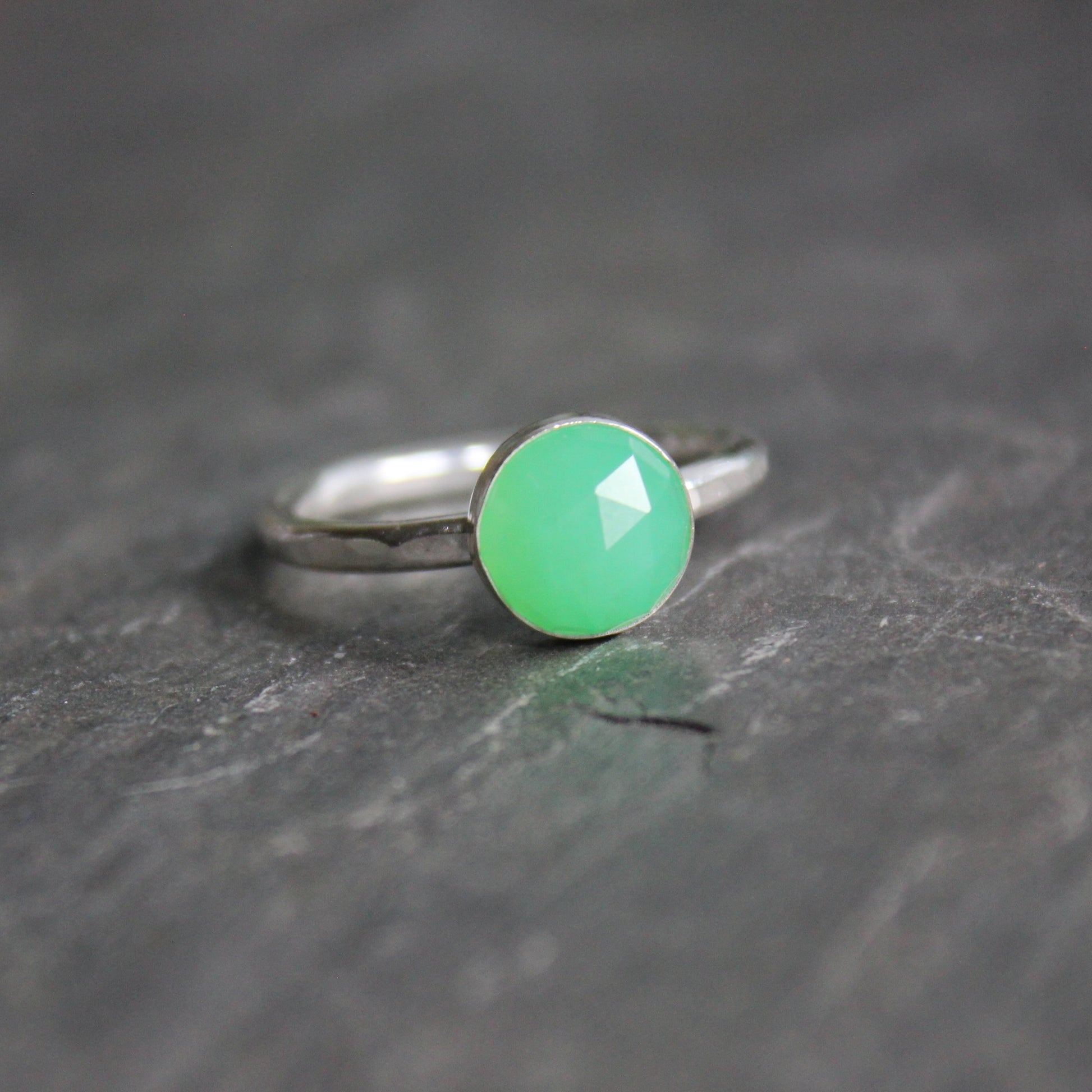 A 8mm rose cut round chrysoprase cabochon set in a sterling silver bezel setting on a sturdy silver band. 