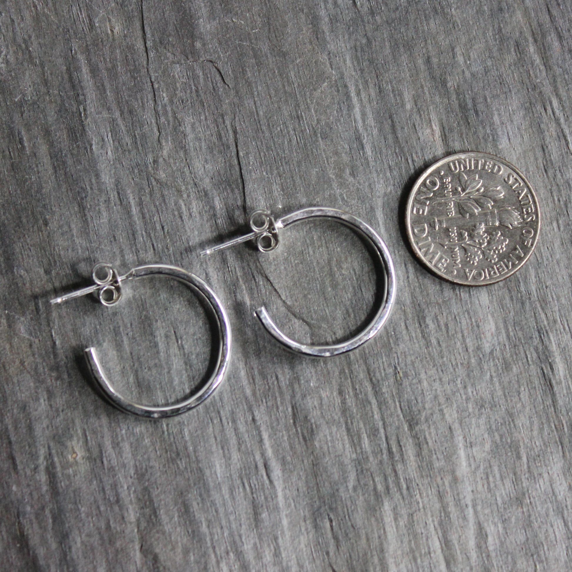 Sterling silver hammered hoops on posts approximately 3/4" in diameter with a bright finish placed next to a similar-sized dime. 