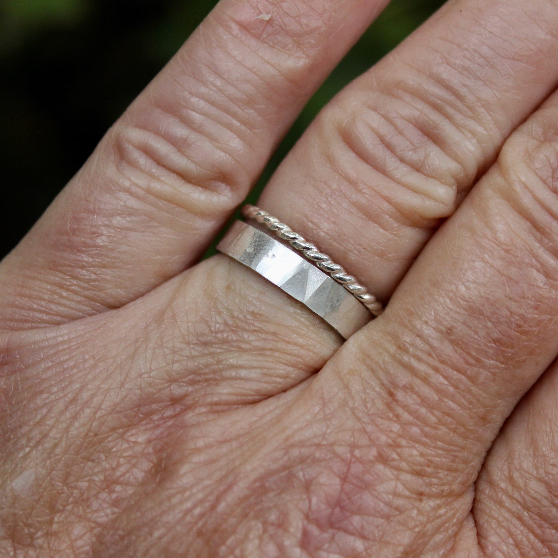 A handmade 4mm wide x 1mm thick flat sterling silver band with a hammered texture and bright finish. Shown with a twisted wire stacking ring. 