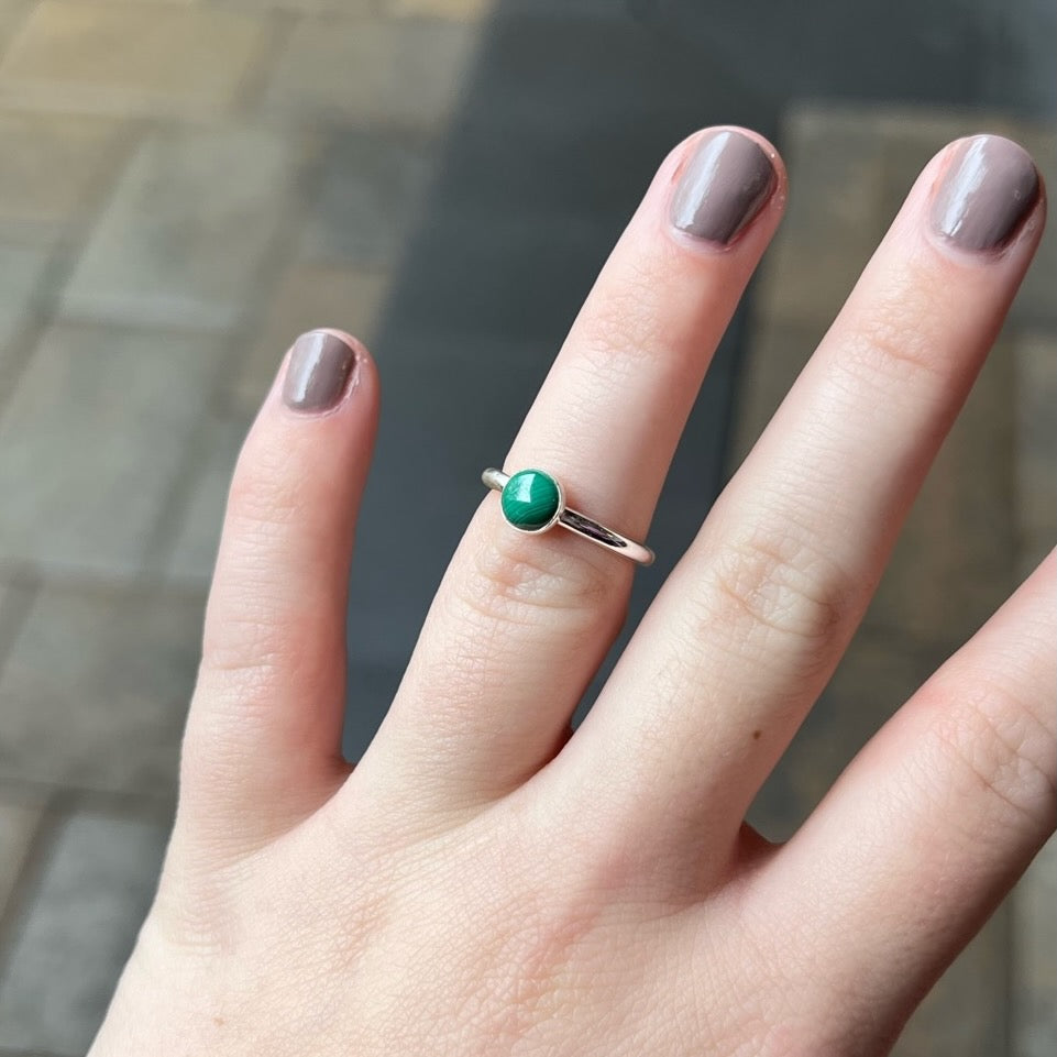 A 6mm round malachite cabochon set in a sterling silver bezel cup on a sturdy silver band modeled on a hand.