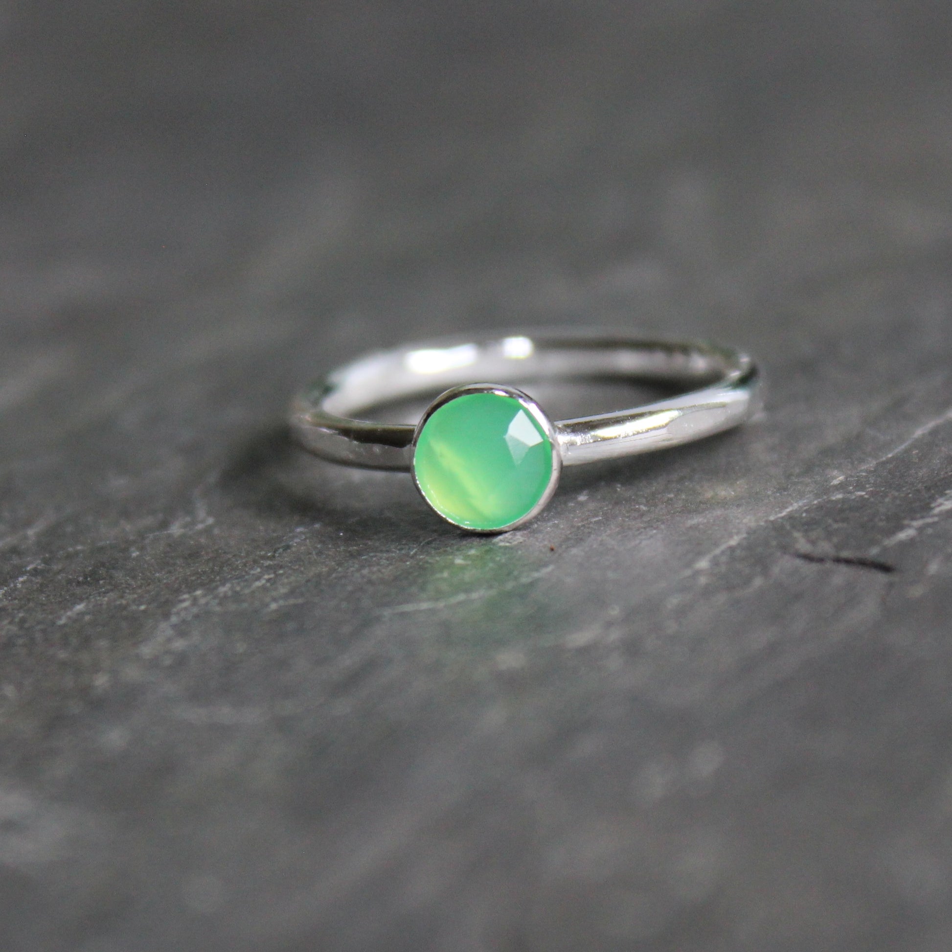 A 6mm rose cut round chrysoprase cabochon set in a sterling silver bezel setting on a sturdy silver band. 