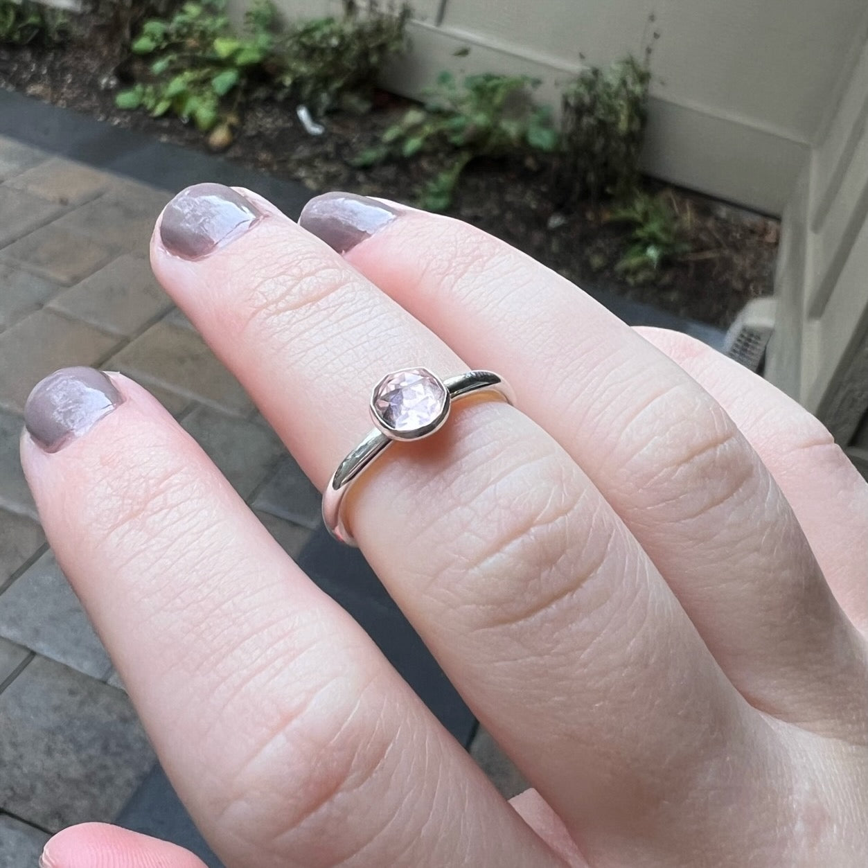 A 6mm round rose cut bezel set morganite gemstone on a sturdy silver band modeled on a finger. 