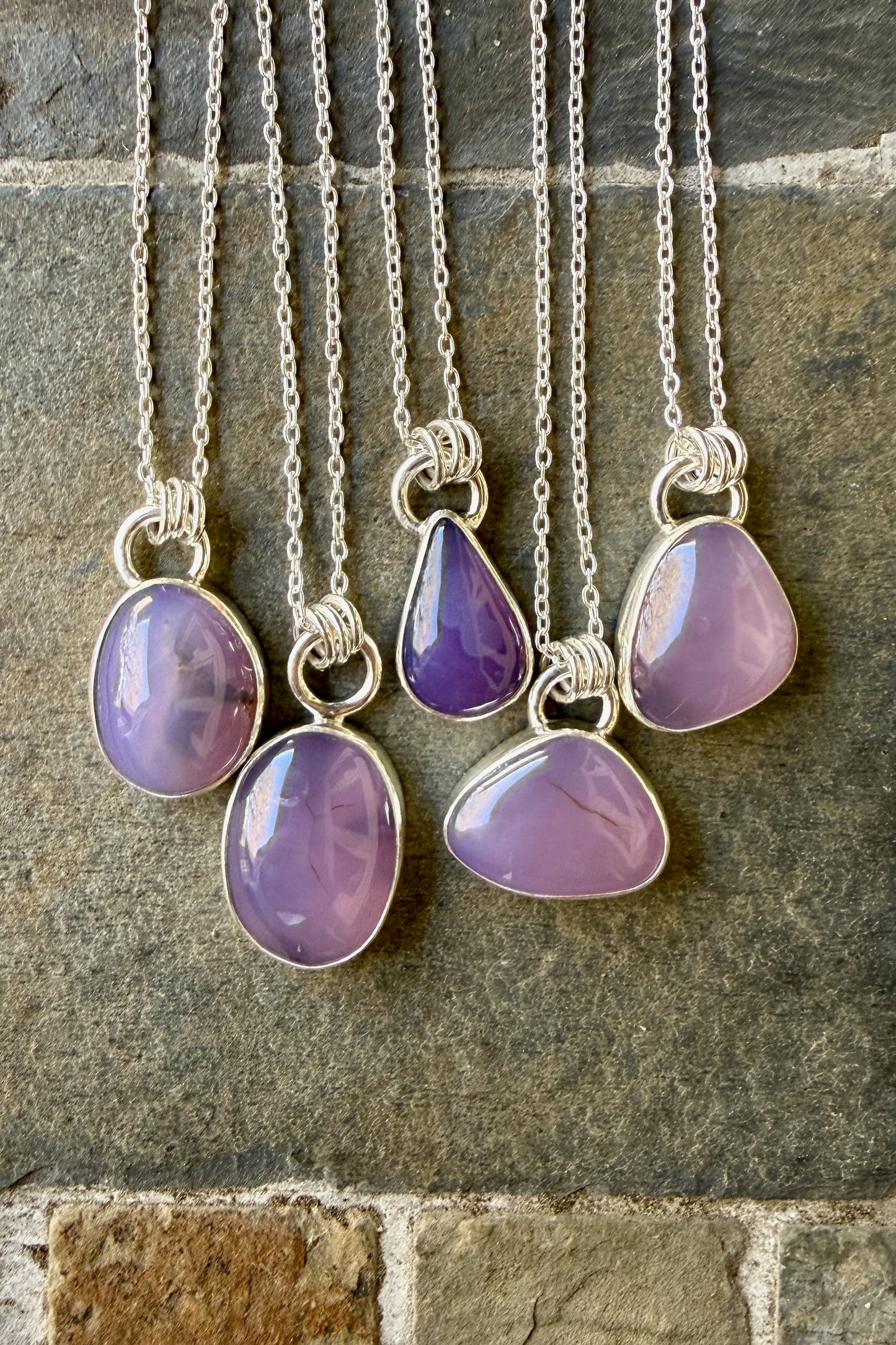 Five silver necklaces with purple holley blue agate pendants on a stone surface