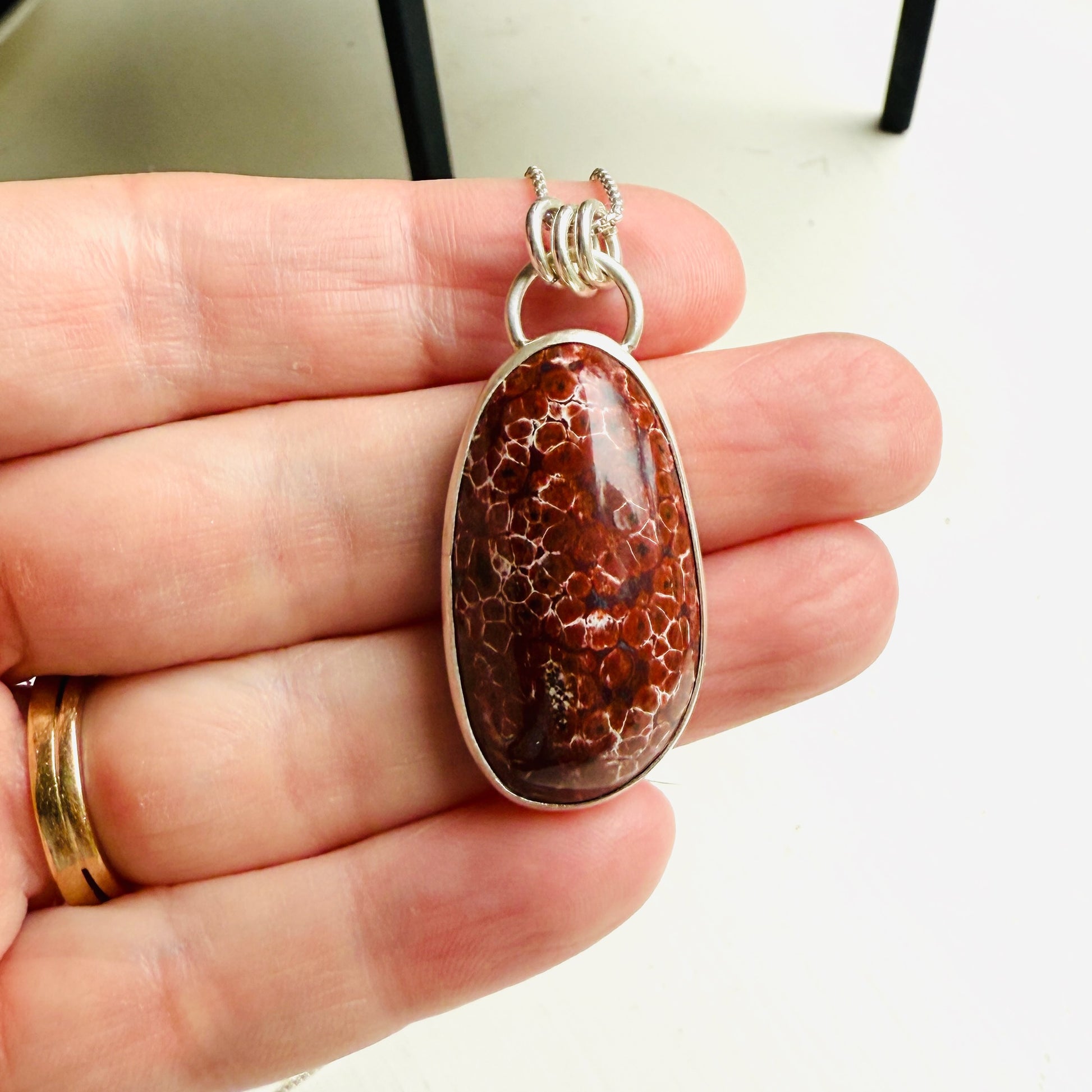 May include: A silver chain necklace with a red and white oval pendant. The pendant is made of a natural stone with a unique pattern.