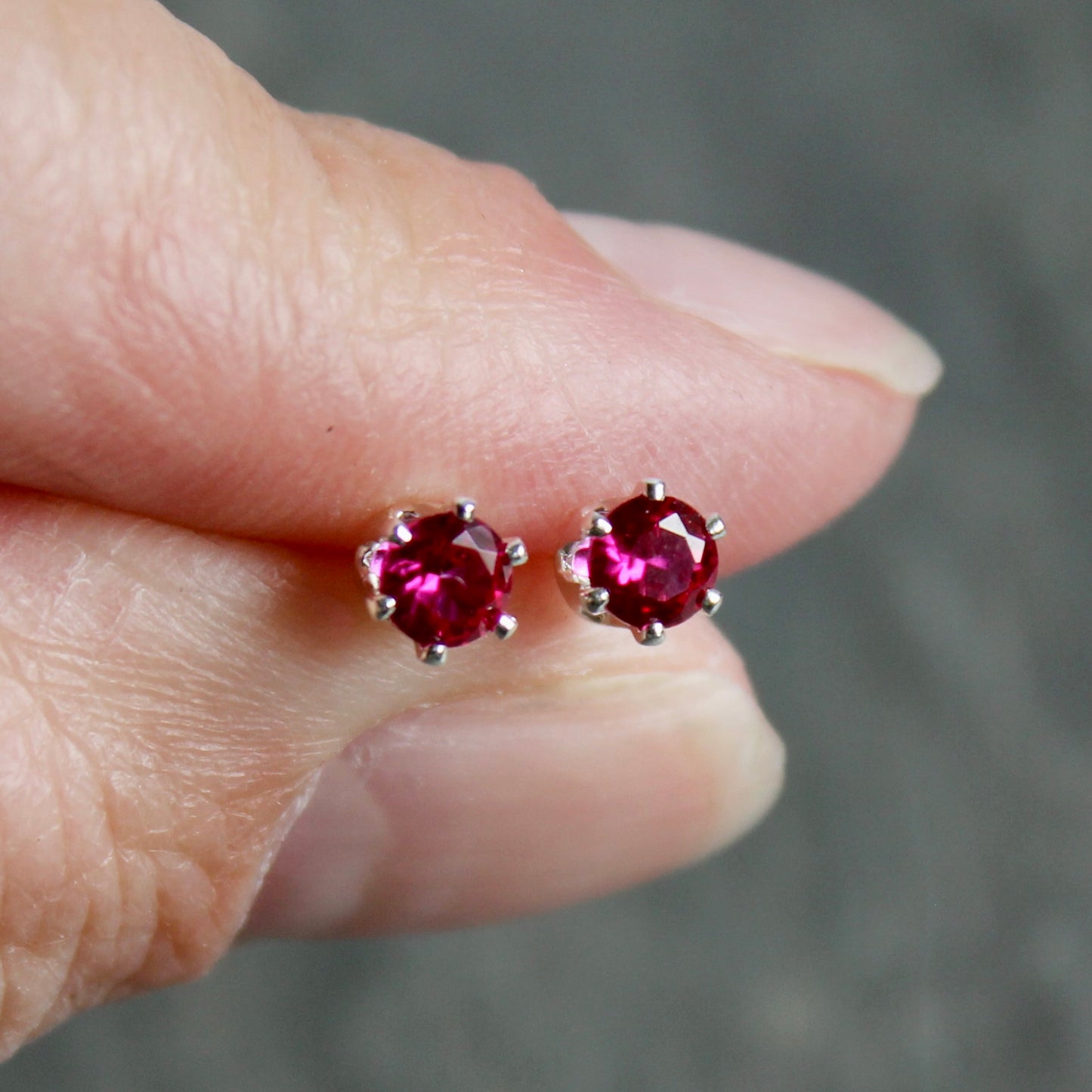 Lab created ruby gemstone stud earrings held between fingers against a blurred background