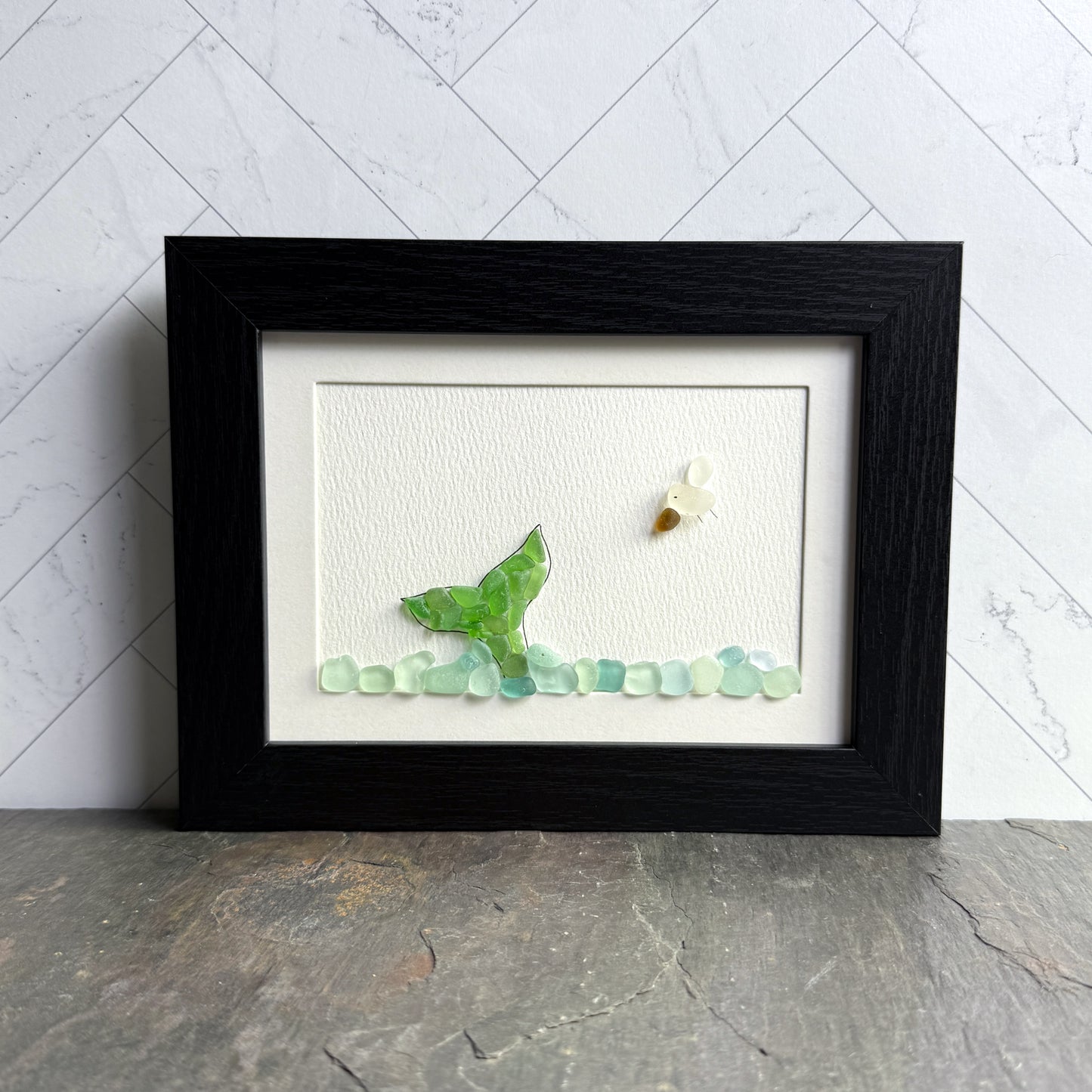 Framed artwork with a green butterfly and small flowers on a white background