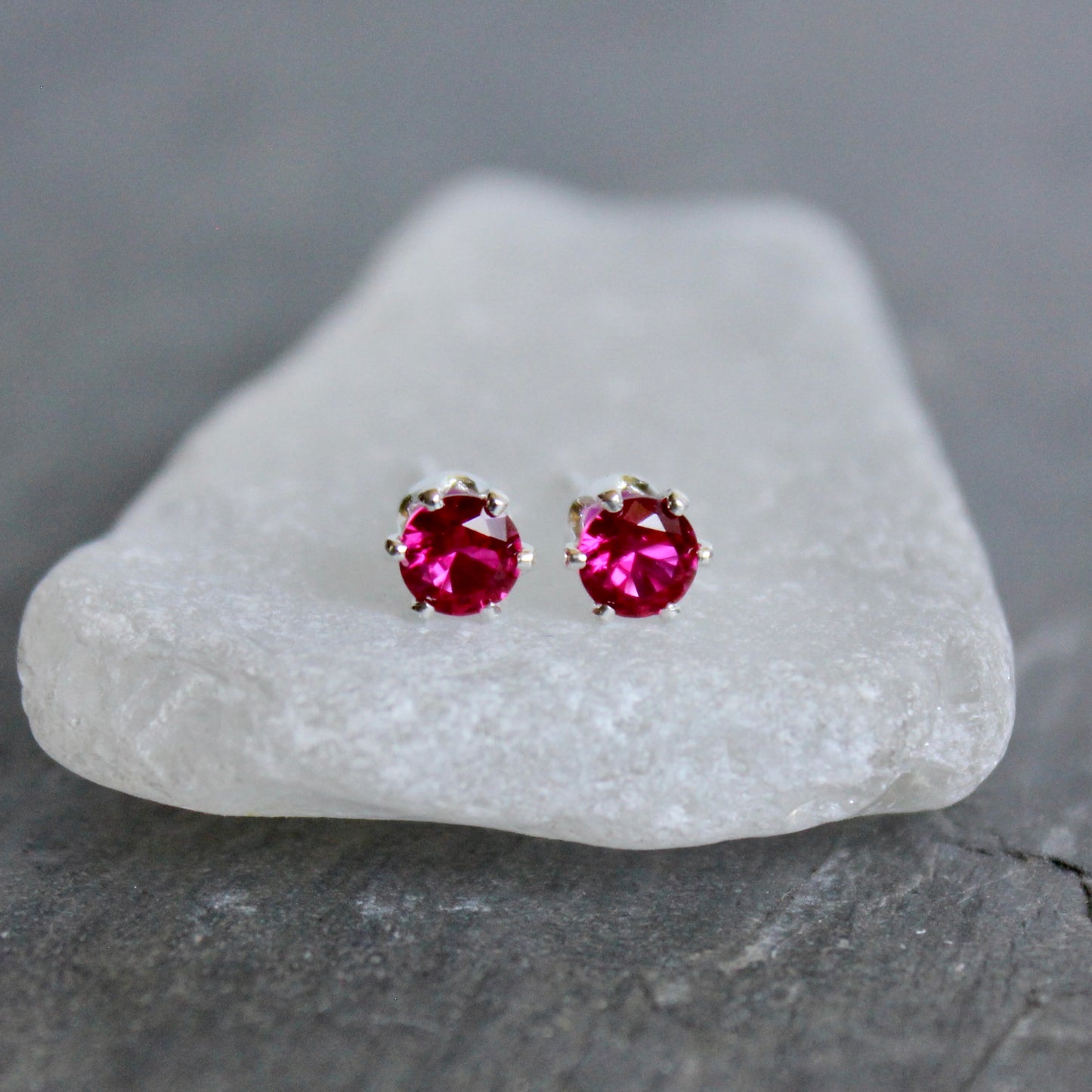Pair of lab created ruby gemstone stud earrings on a white stone with a gray background