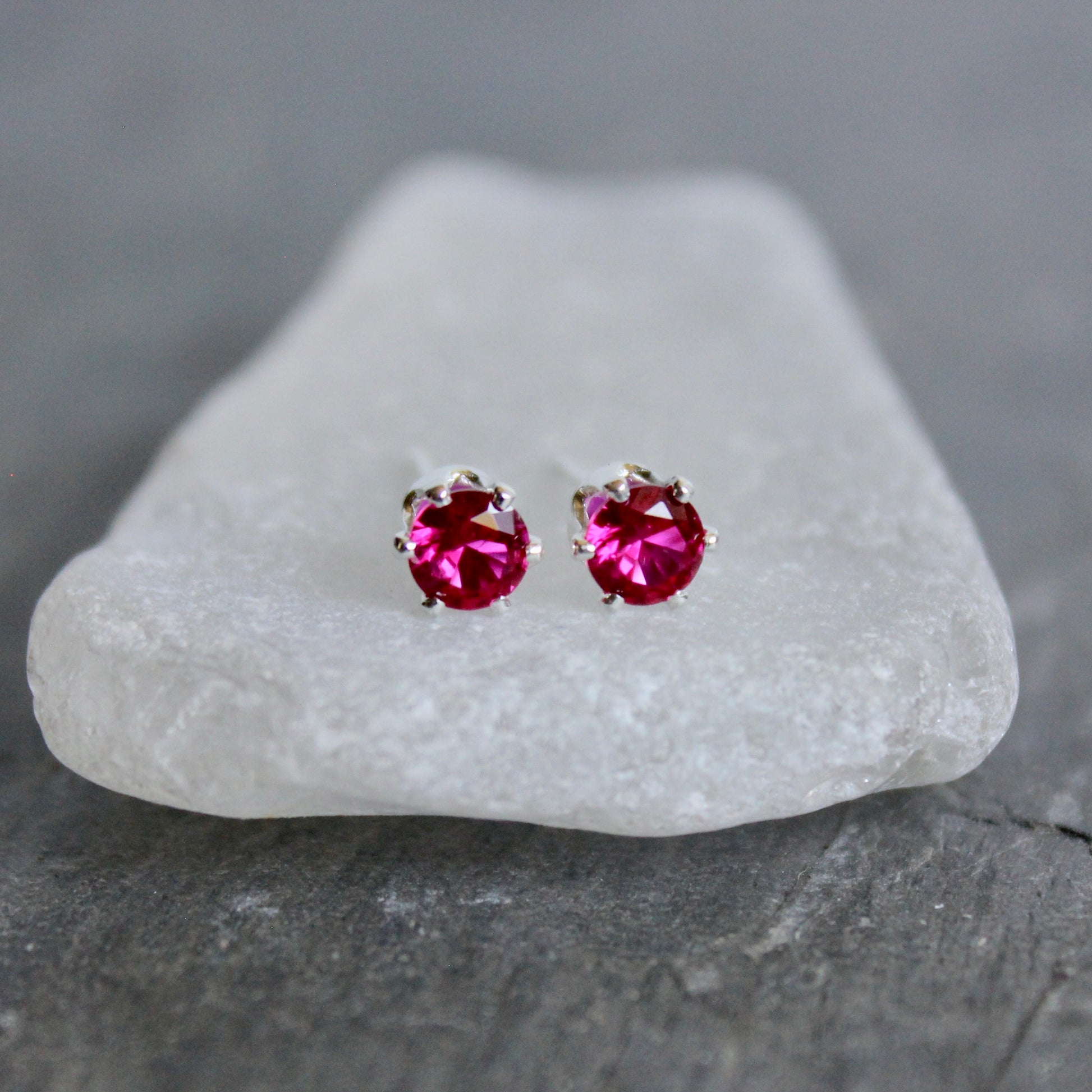 Pair of pink gemstone stud earrings on a white stone with a gray background