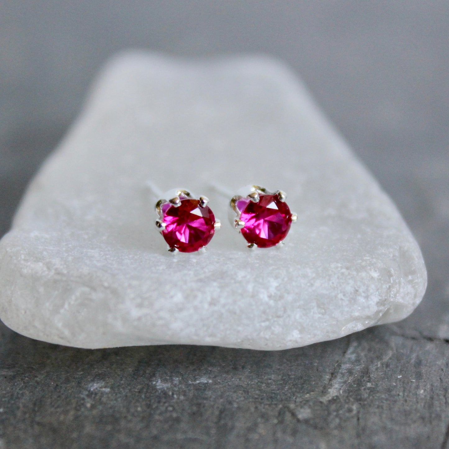Pair of lab created ruby gemstone stud earrings on a white stone surface