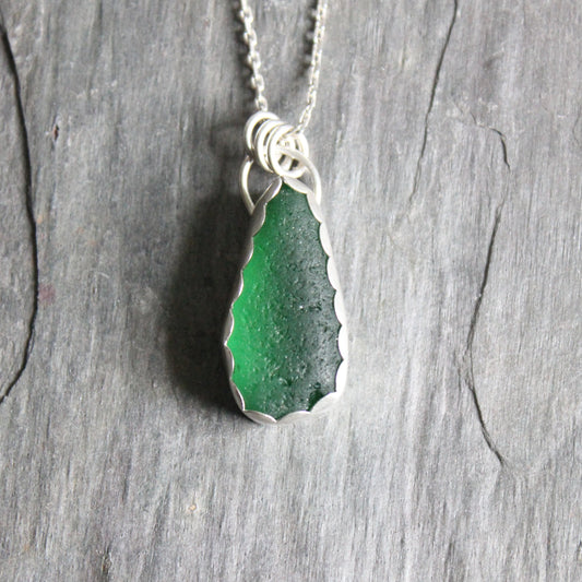 This is a large chunky piece of dark emerald green sea glass set in a fine and sterling silver scalloped bezel setting. 