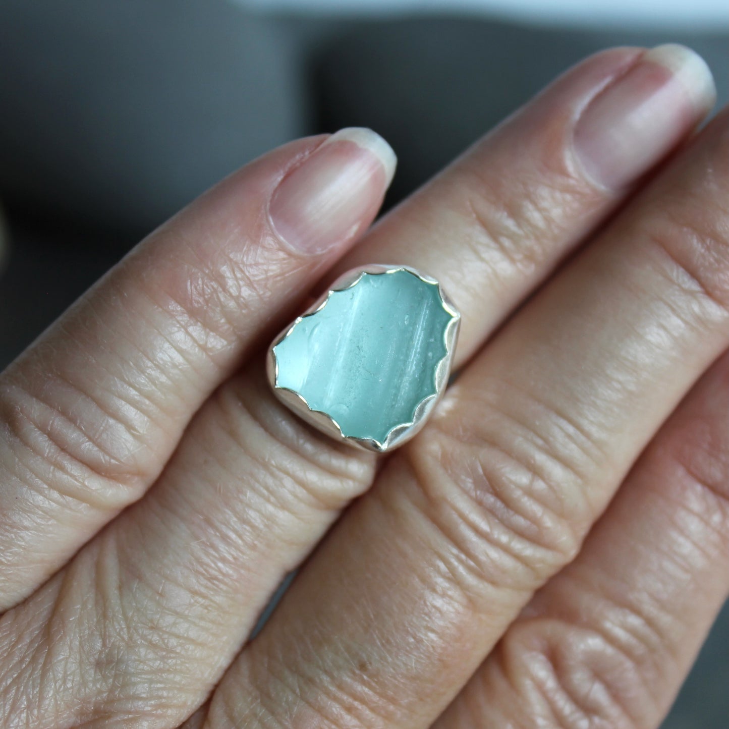 This statement ring has a pale aqua blue piece of sea glass that is set in a fine and sterling silver scalloped bezel on a sturdy hammered band. This piece is actually from a bottle neck. Handmade by Barb Macy in Corvallis, OR. Size 5
