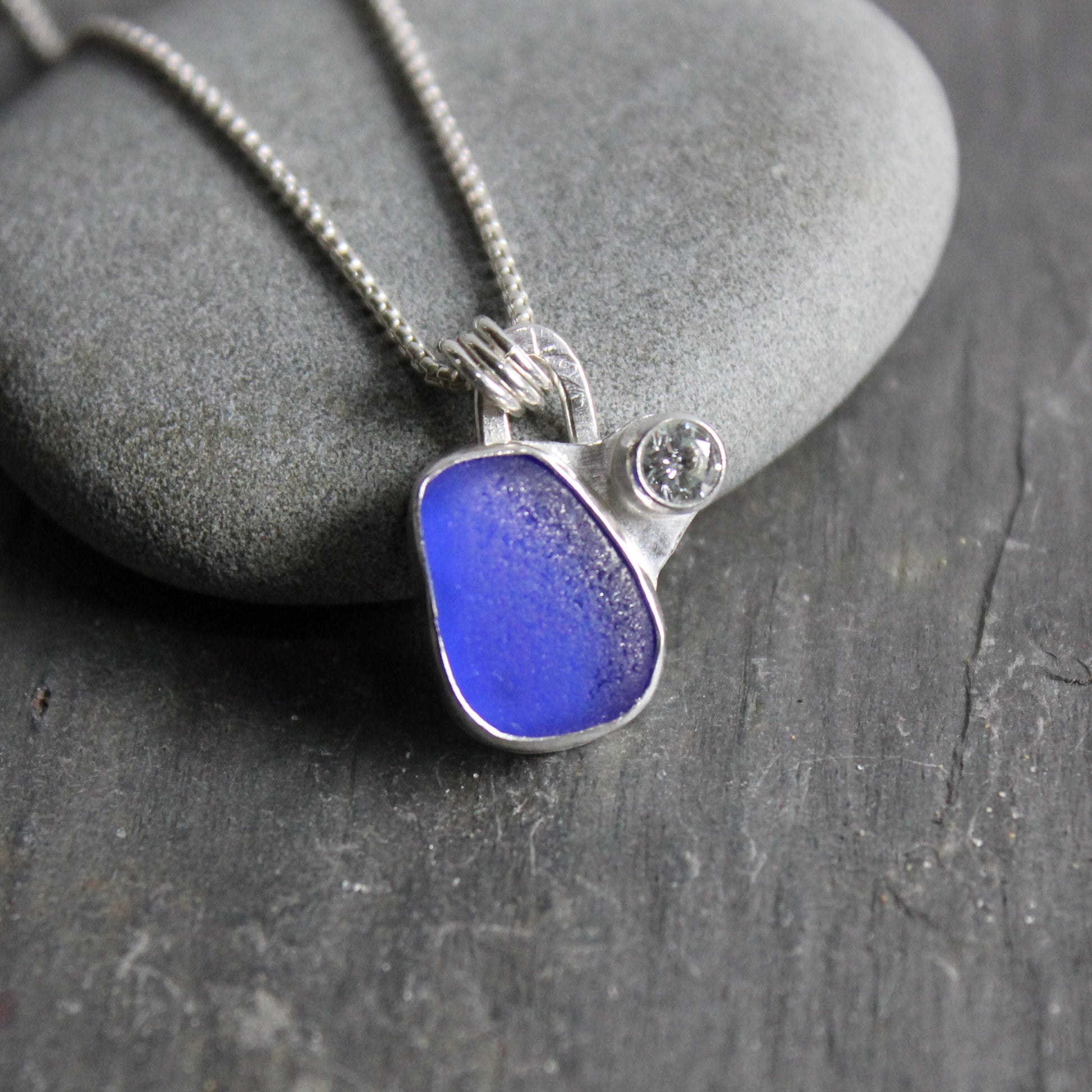 This necklace has a small piece of cobalt blue sea glass set in a fine and sterling silver bezel setting, accented with a tube set cubic zirconia on a sterling silver chain. 