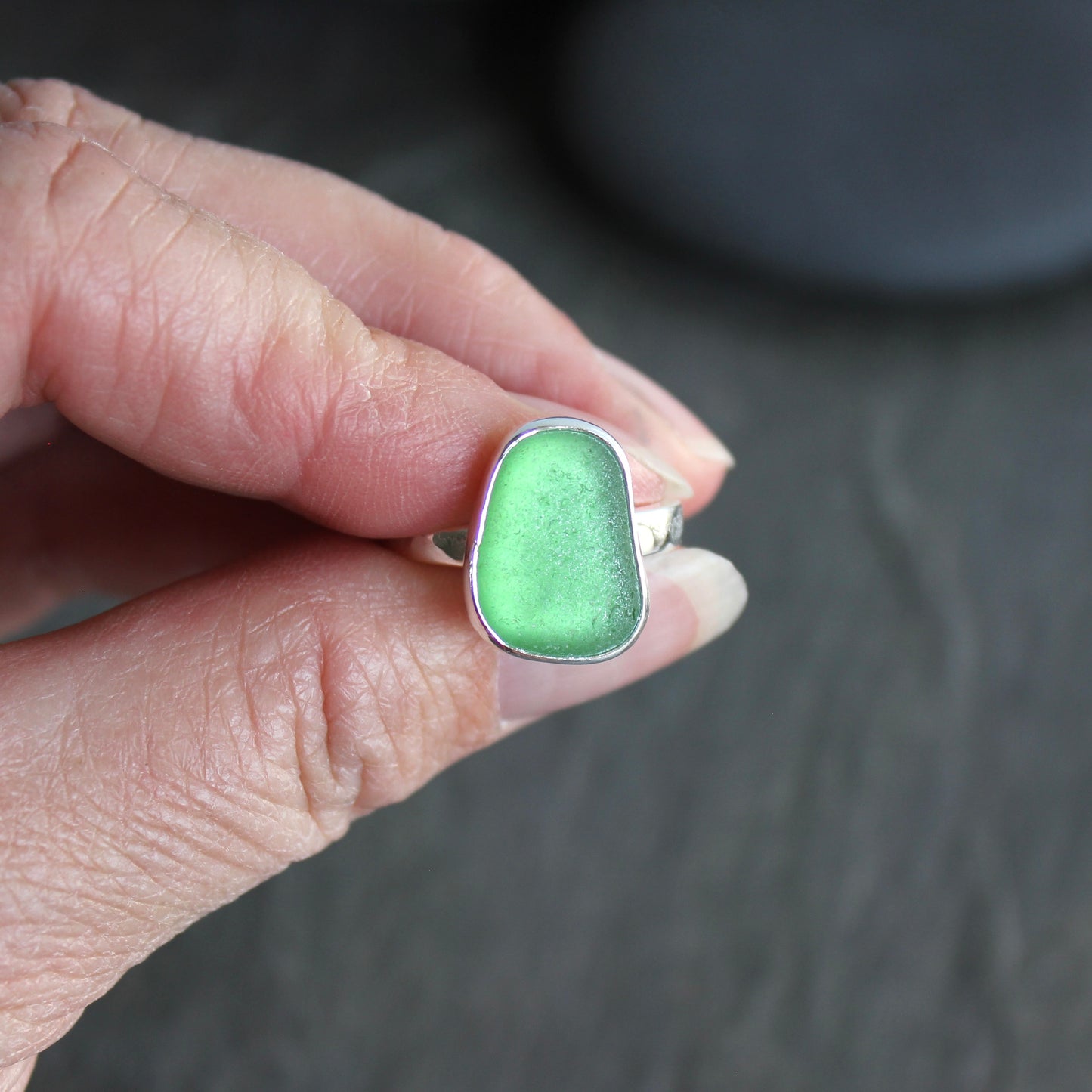 Green ring with silver setting held by a hand on a dark background