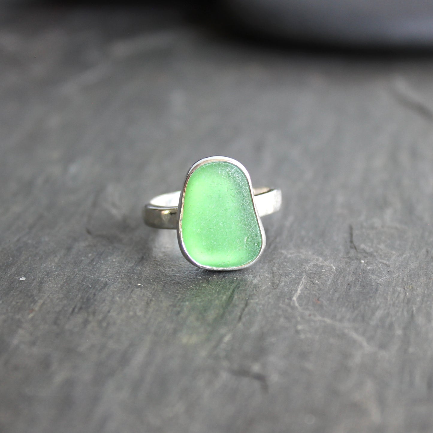 Green ring with silver setting on a dark gray surface