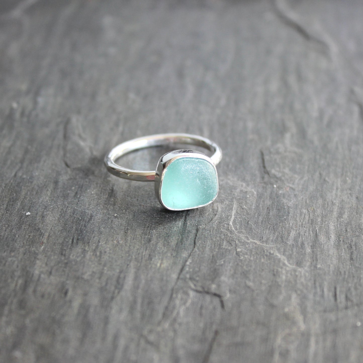 Silver ring with a light blue gemstone on a dark wooden surface