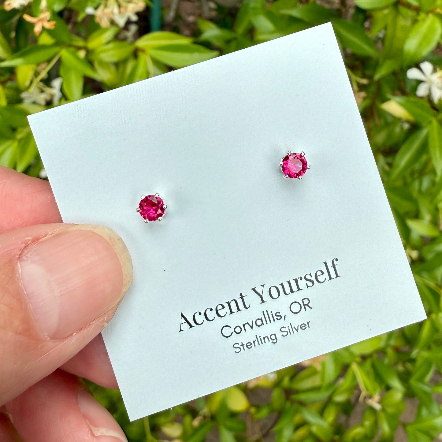 Lab created ruby stud earrings on a card held by a hand with a green leafy background