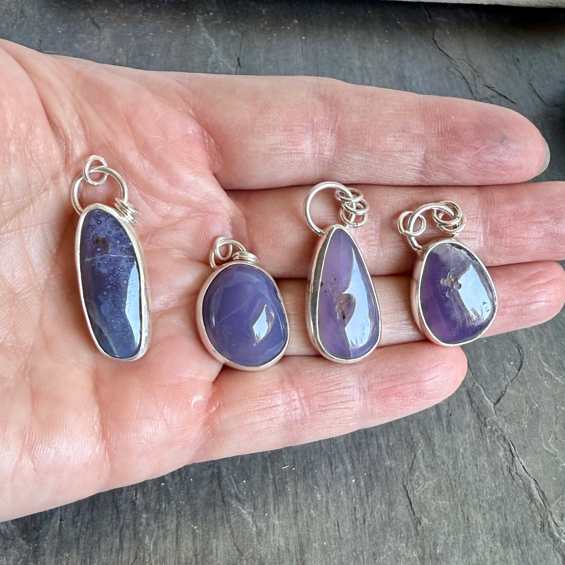 Four purple teardrop pendants with silver settings on a hand. A long holley blue agate cabochon set in a fine and sterling silver bezel setting on a sturdy silver chain.