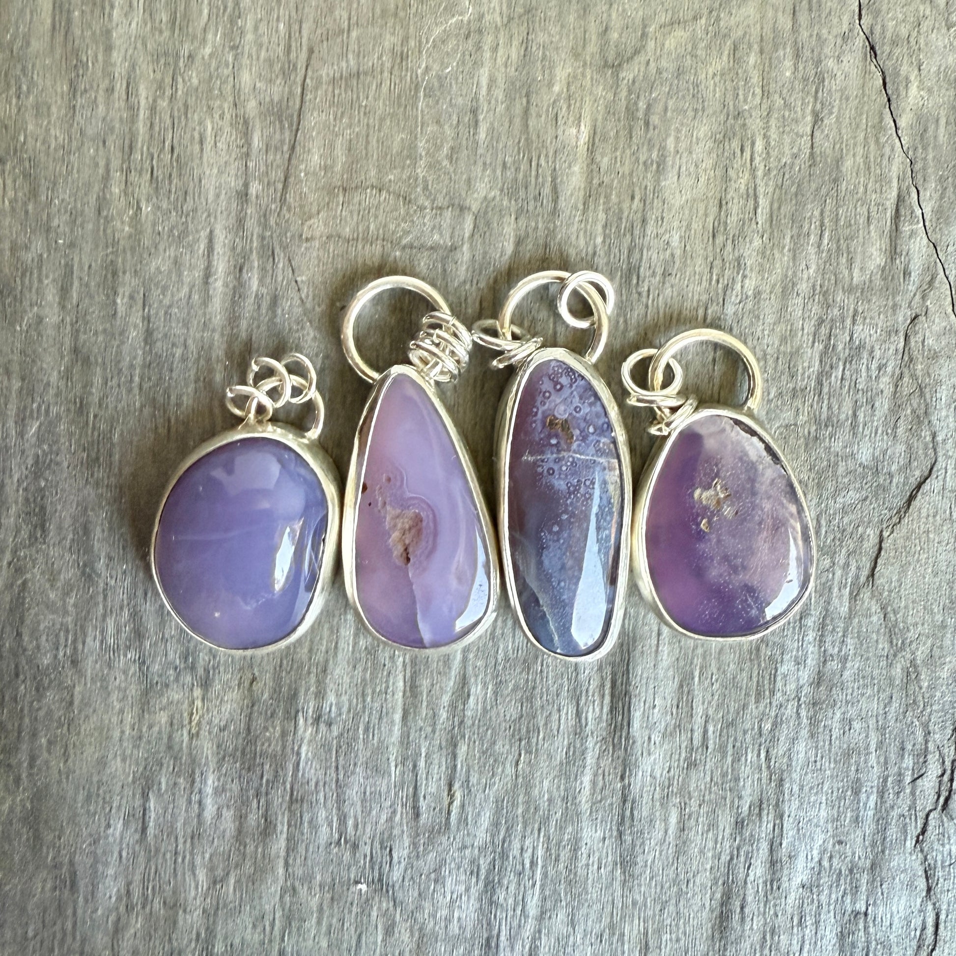 Four purple teardrop pendants with silver loops on a wooden surface. A long holley blue agate cabochon set in a fine and sterling silver bezel setting on a sturdy silver chain.