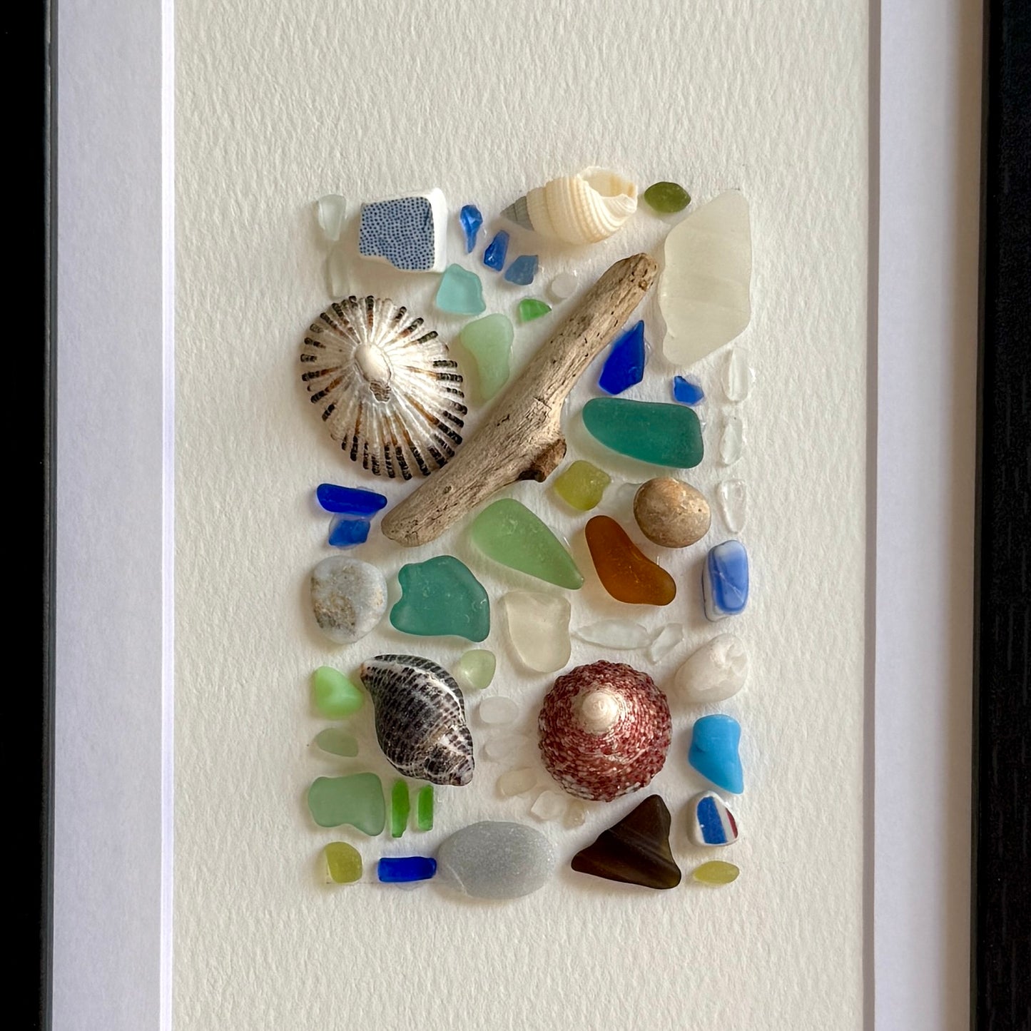 Decorative piece with seaglass, shells, and driftwood on a white background