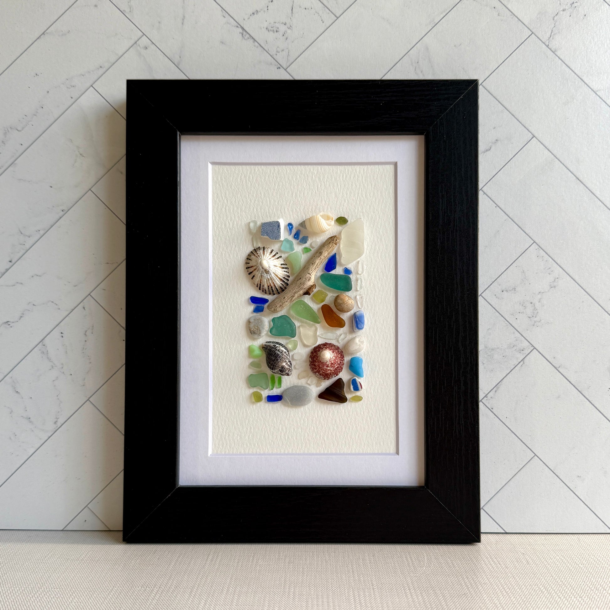 Framed artwork with sea glass and shells on a white background