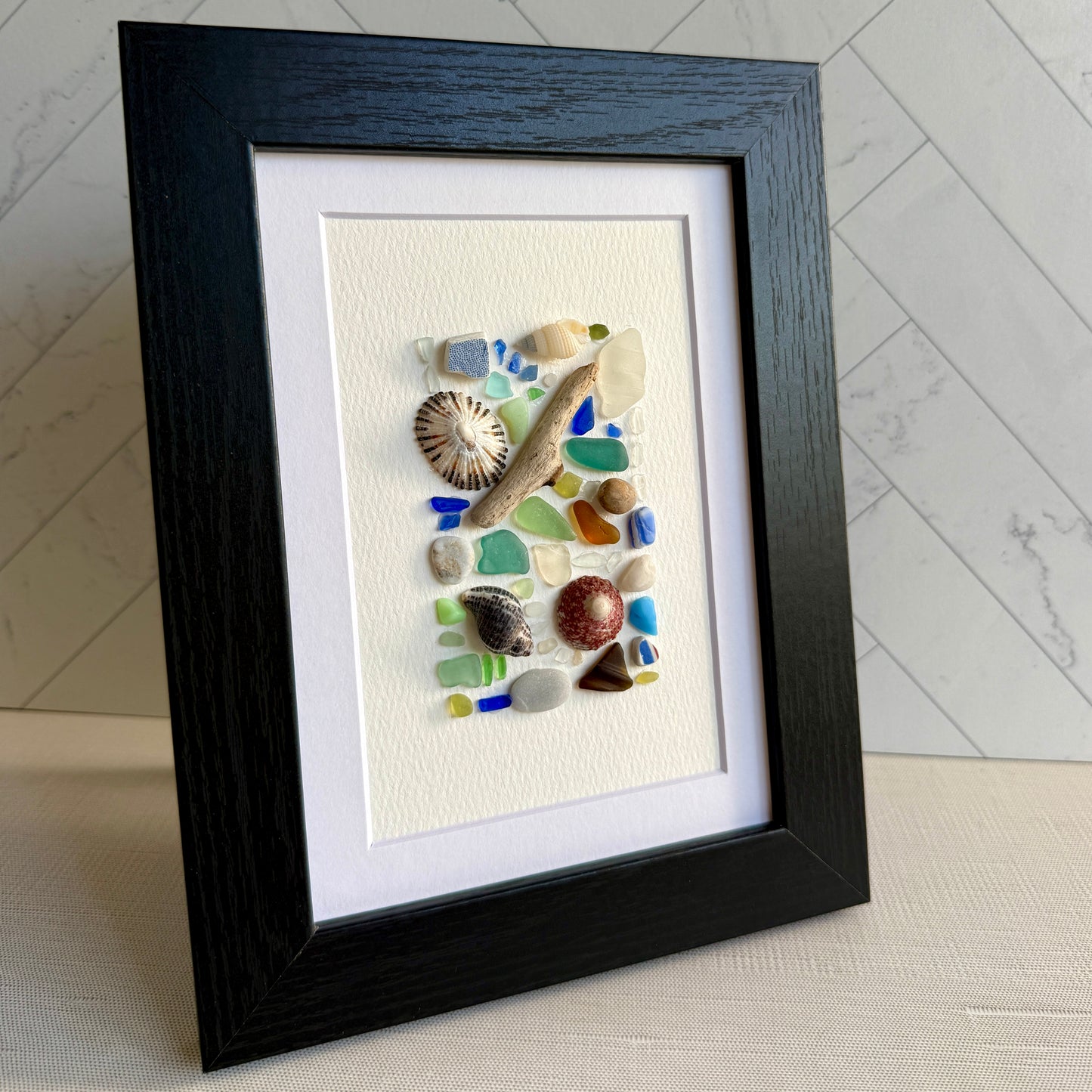 Framed artwork with seashells and sea glass pieces on a white background
