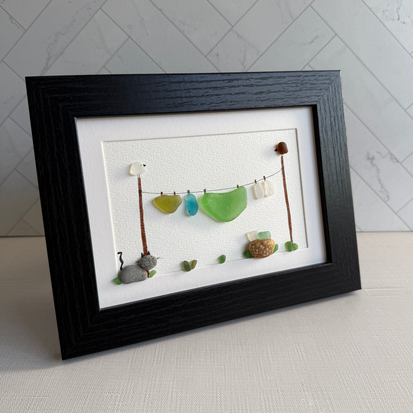 Framed artwork of a cat and laundry on a line with a black frame.