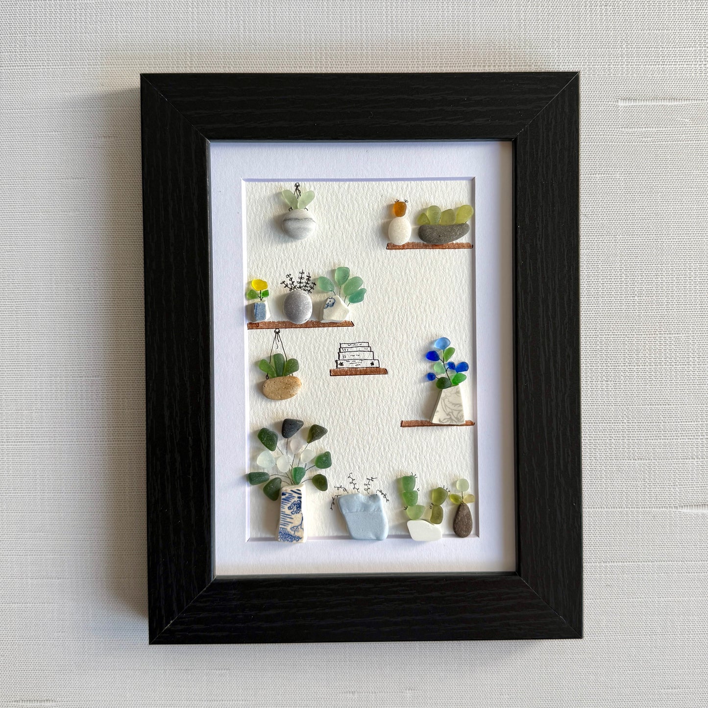 Framed artwork of a miniature garden with various plants on a textured wall.