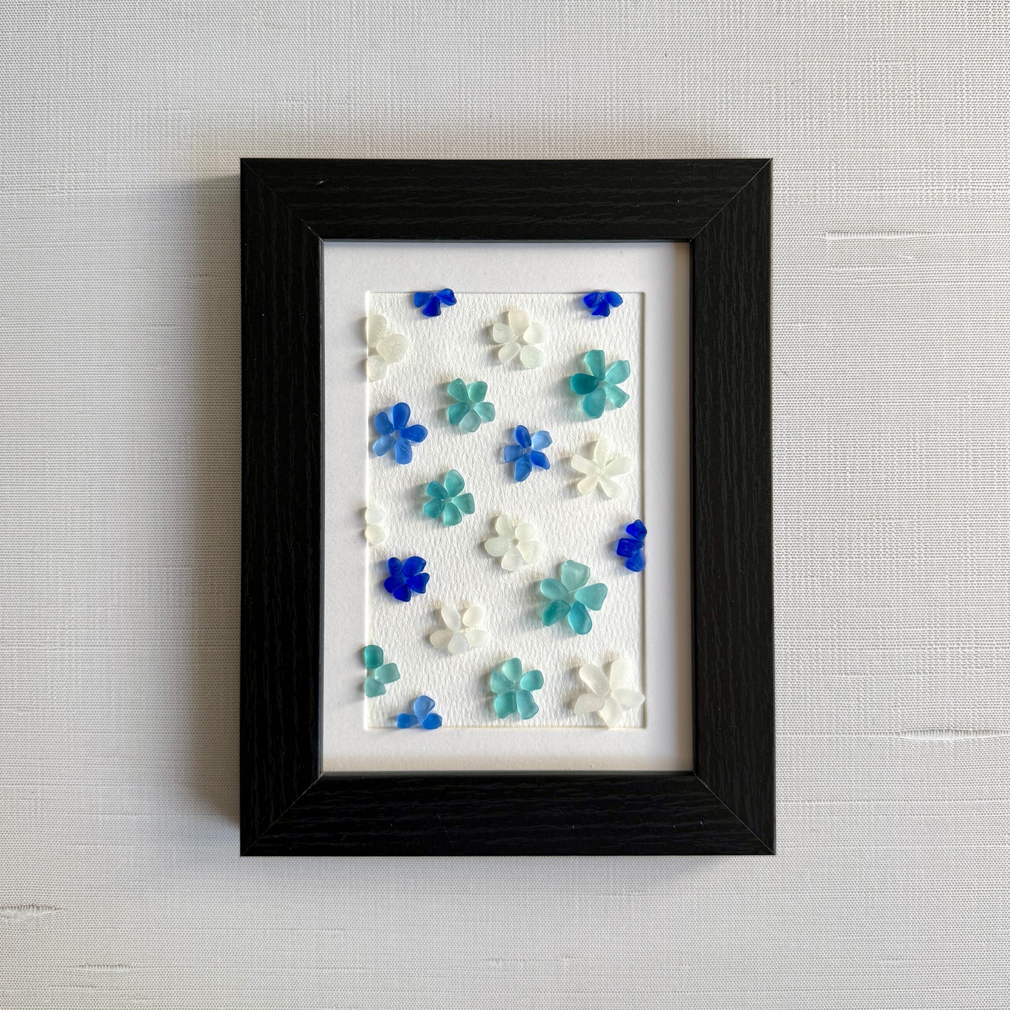 Framed artwork with colorful flower-shaped objects on a textured wall.