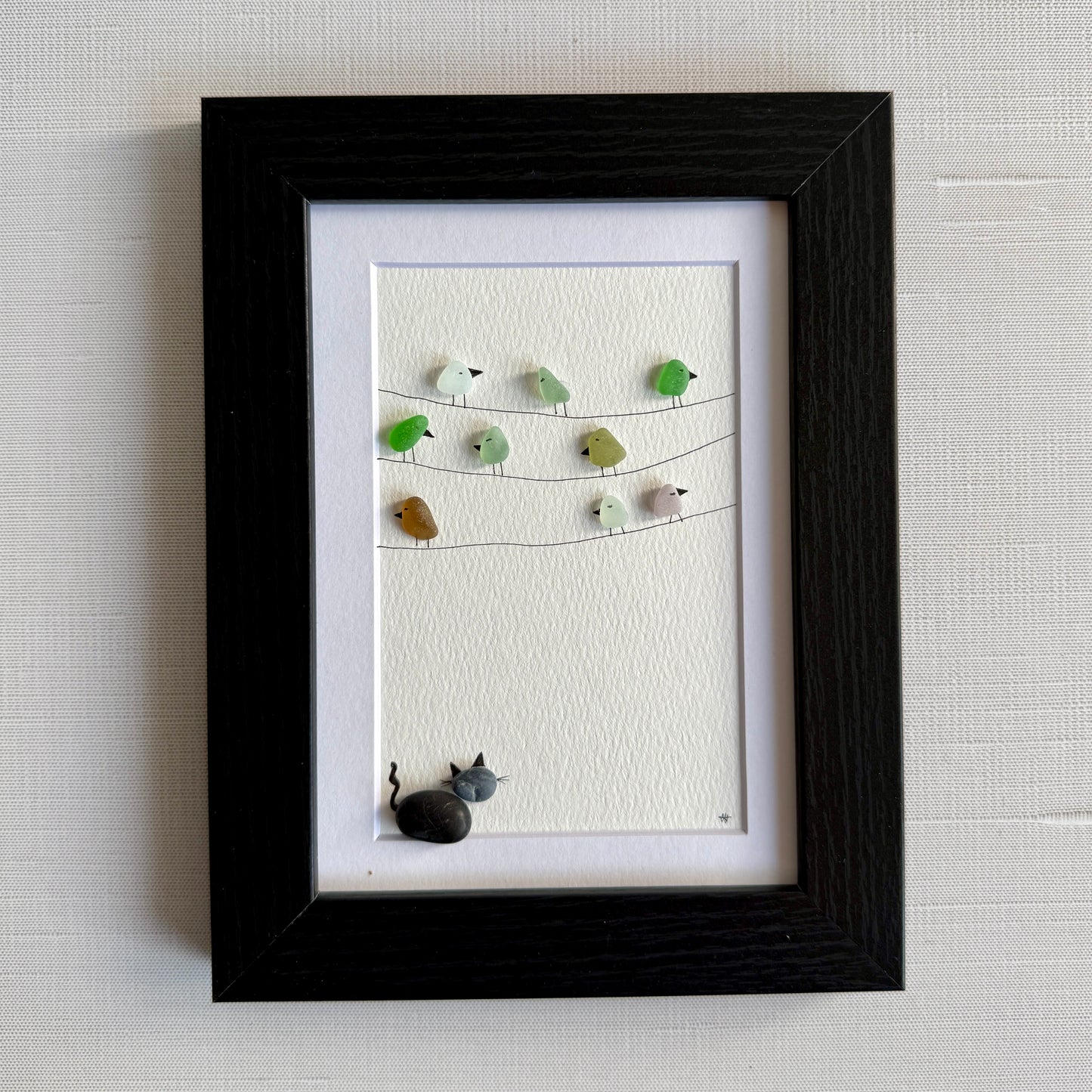 Framed sea glass artwork with birds and a pebble cat on a white background