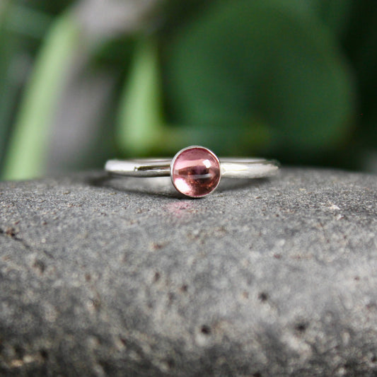 An approximately 6mm pink tourmaline cabochon set in a sterling silver bezel setting on a sturdy hammered band. 