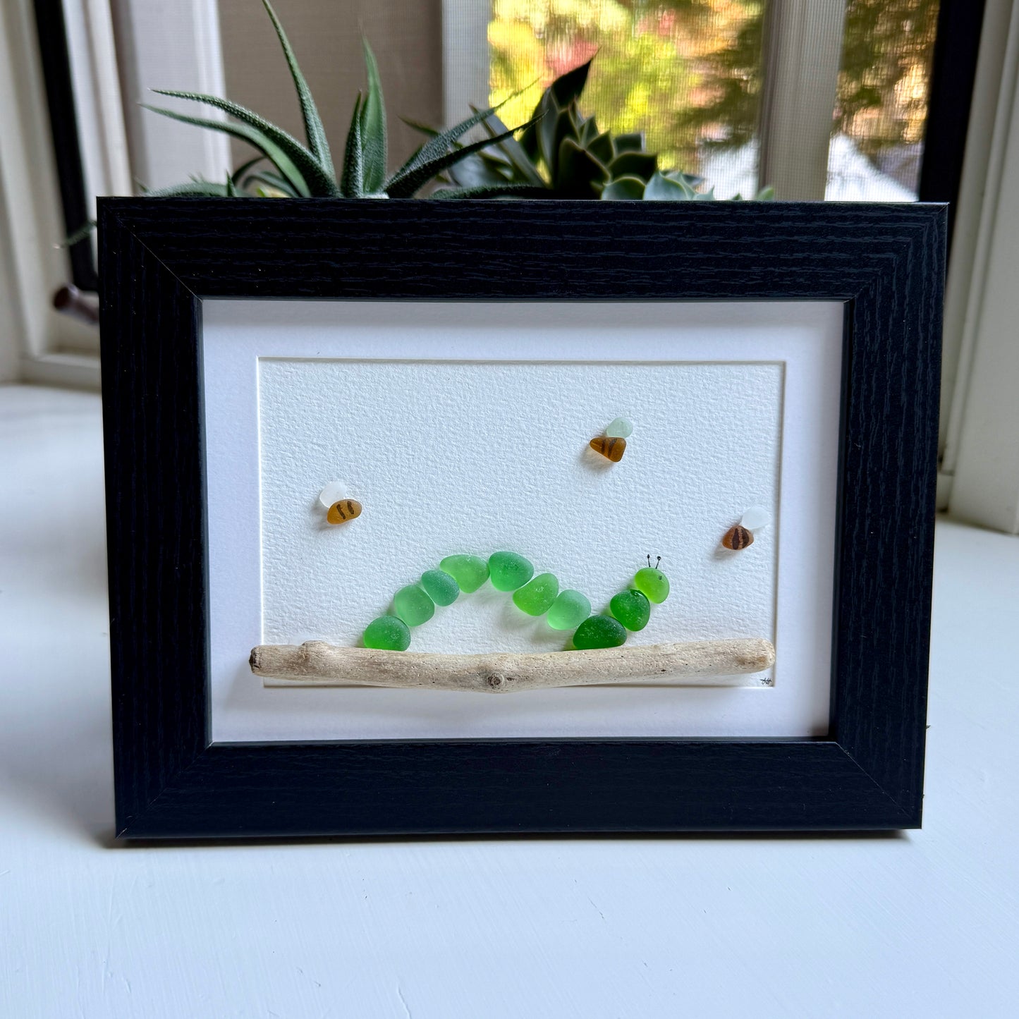 Framed artwork with a green caterpillar and small insects on a white background