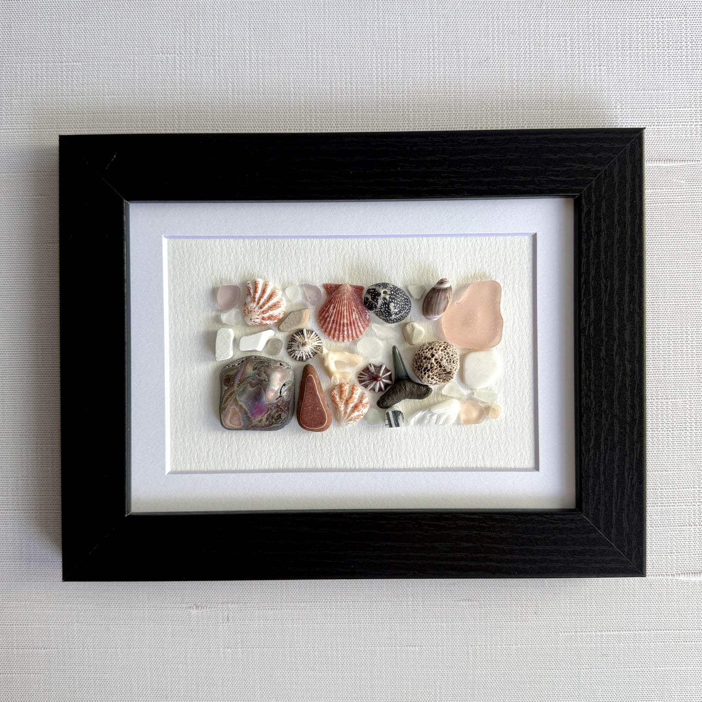 Framed artwork with sea glass and shells on a white background
