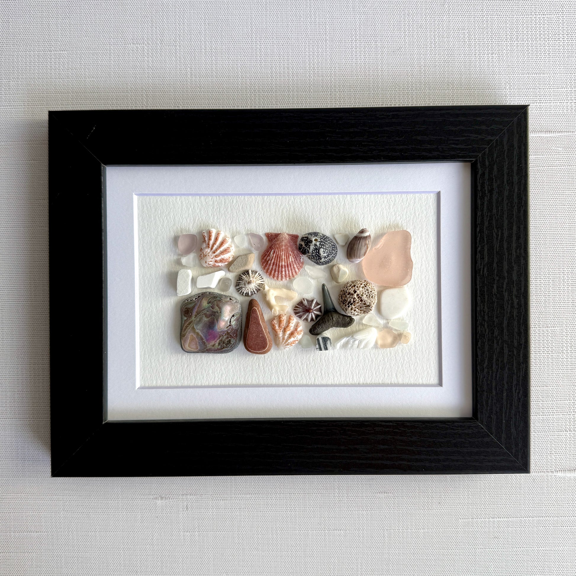 Framed artwork with sea glass and shells on a white background
