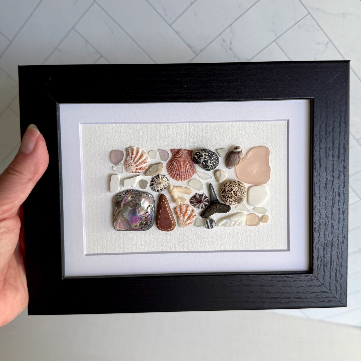 Framed artwork with sea glass and shells on a white background