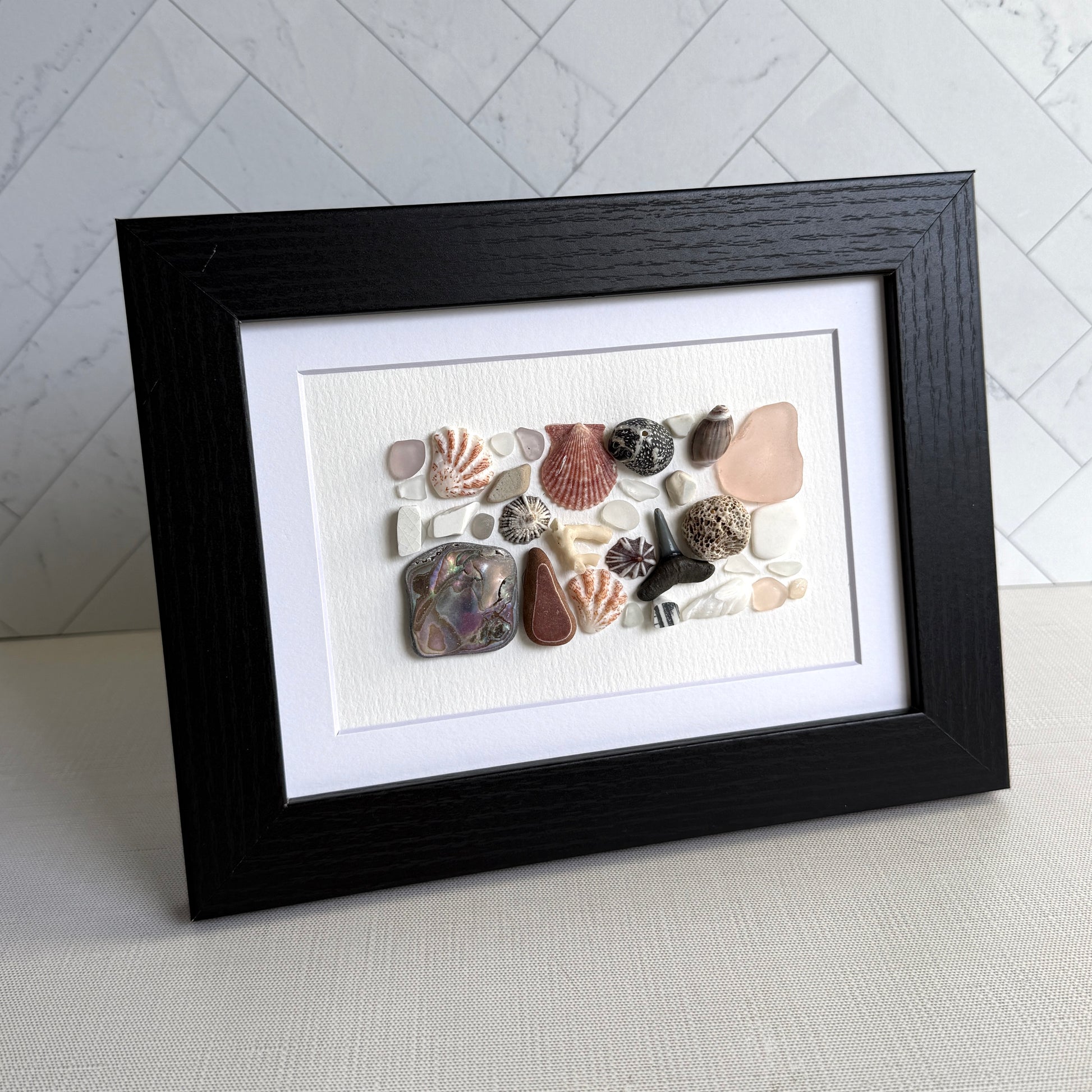 Framed artwork with sea glass and shells on a white background