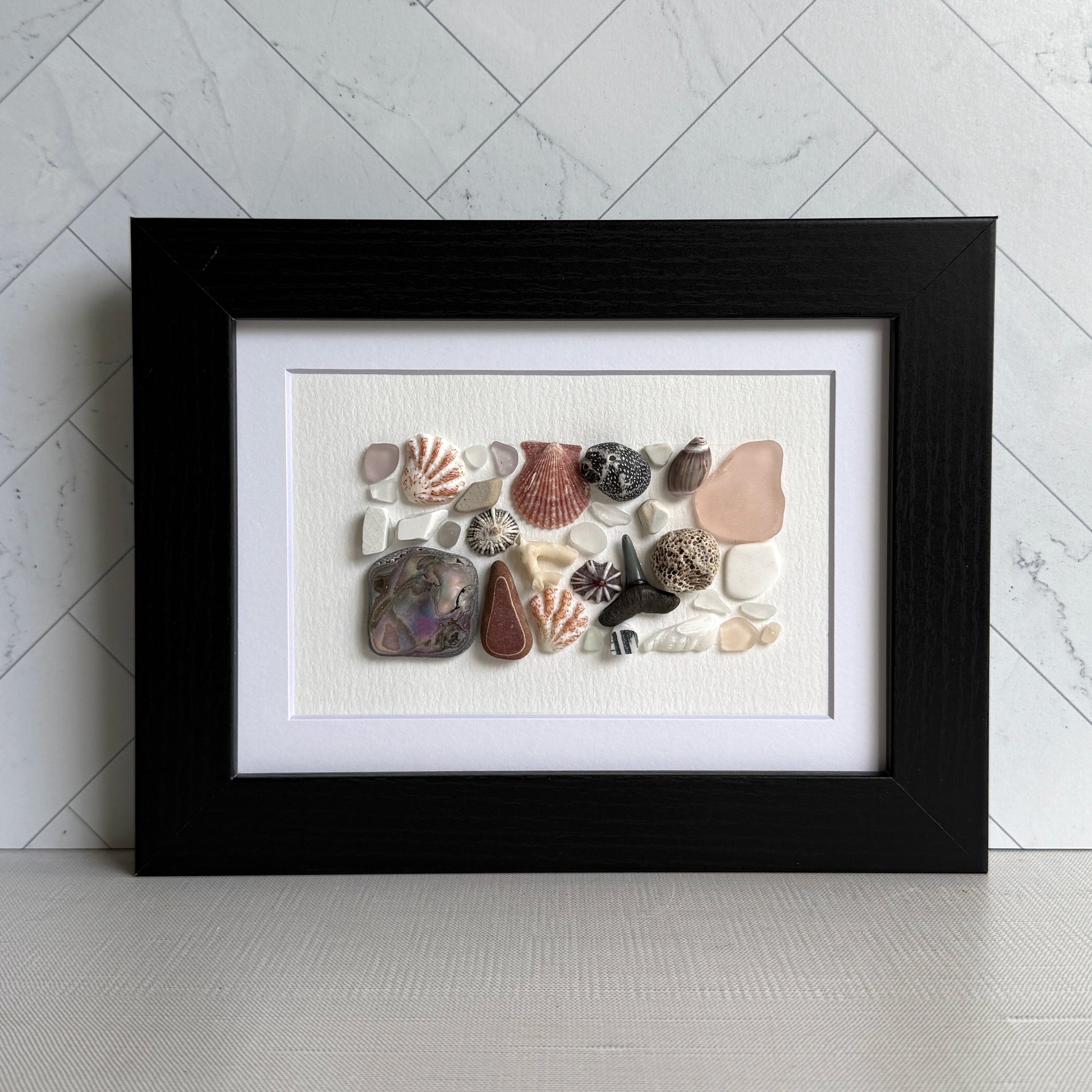 Framed artwork with sea glass and shells on a white background
