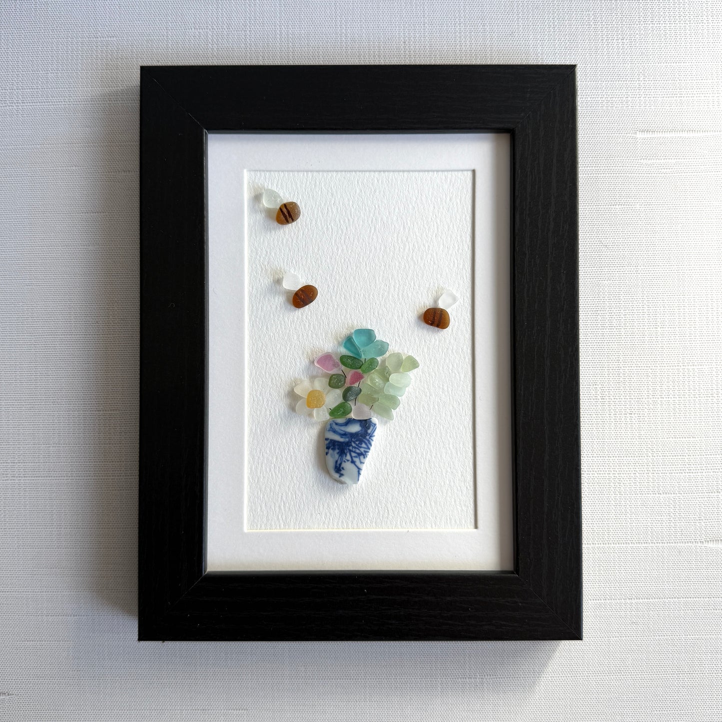 Framed artwork made from small stones and beads on a white background