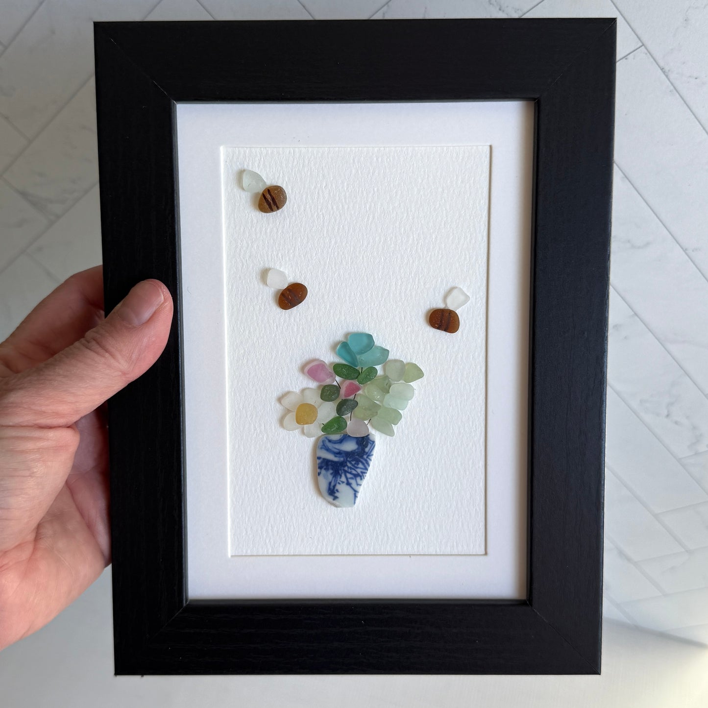 Framed artwork of a vase with flowers made from seashells on a white background