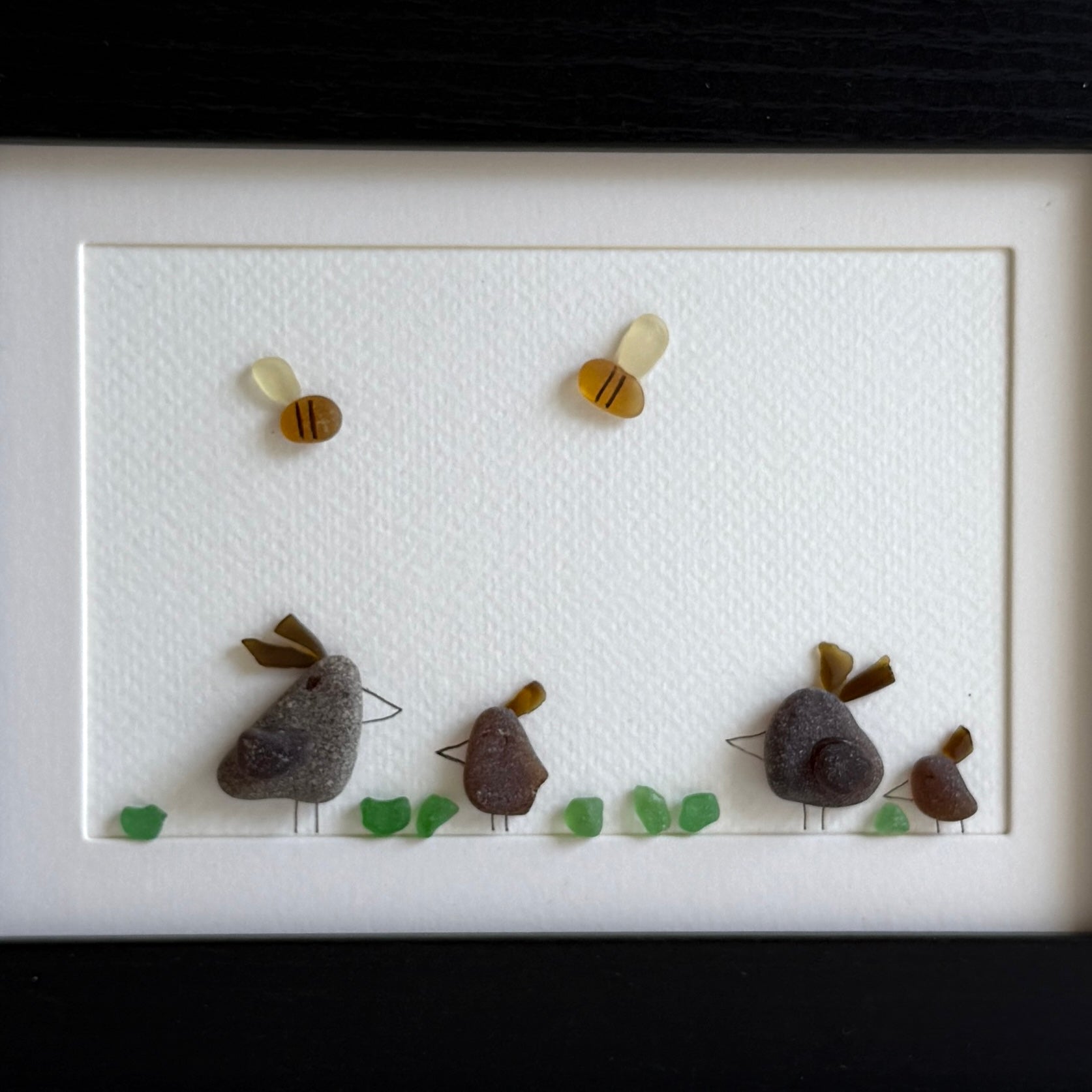 Framed sea glass artwork of hens and chickens on a white background with a black frame.
