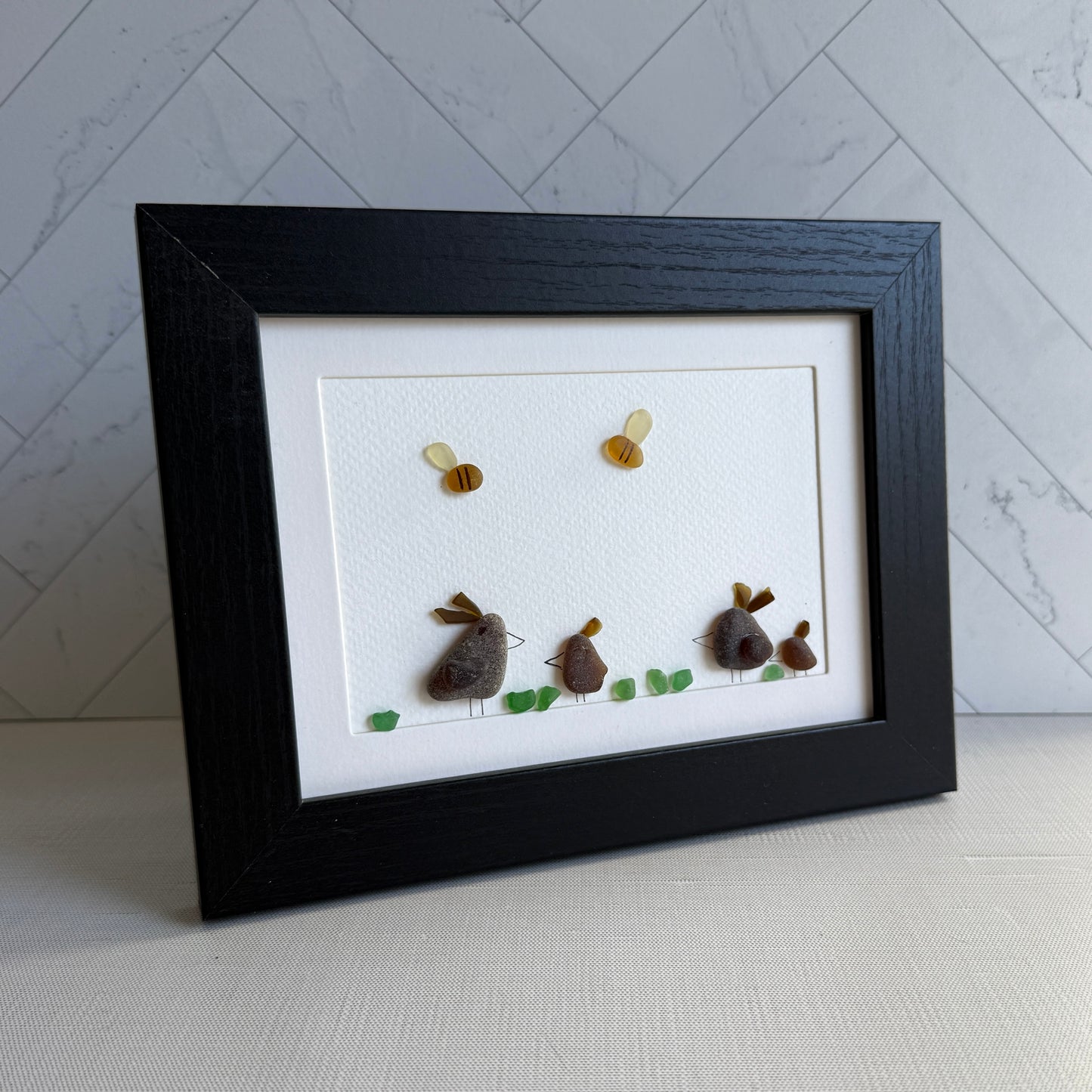 Framed sea glass artwork of hens and chickens on a white background with a black frame.