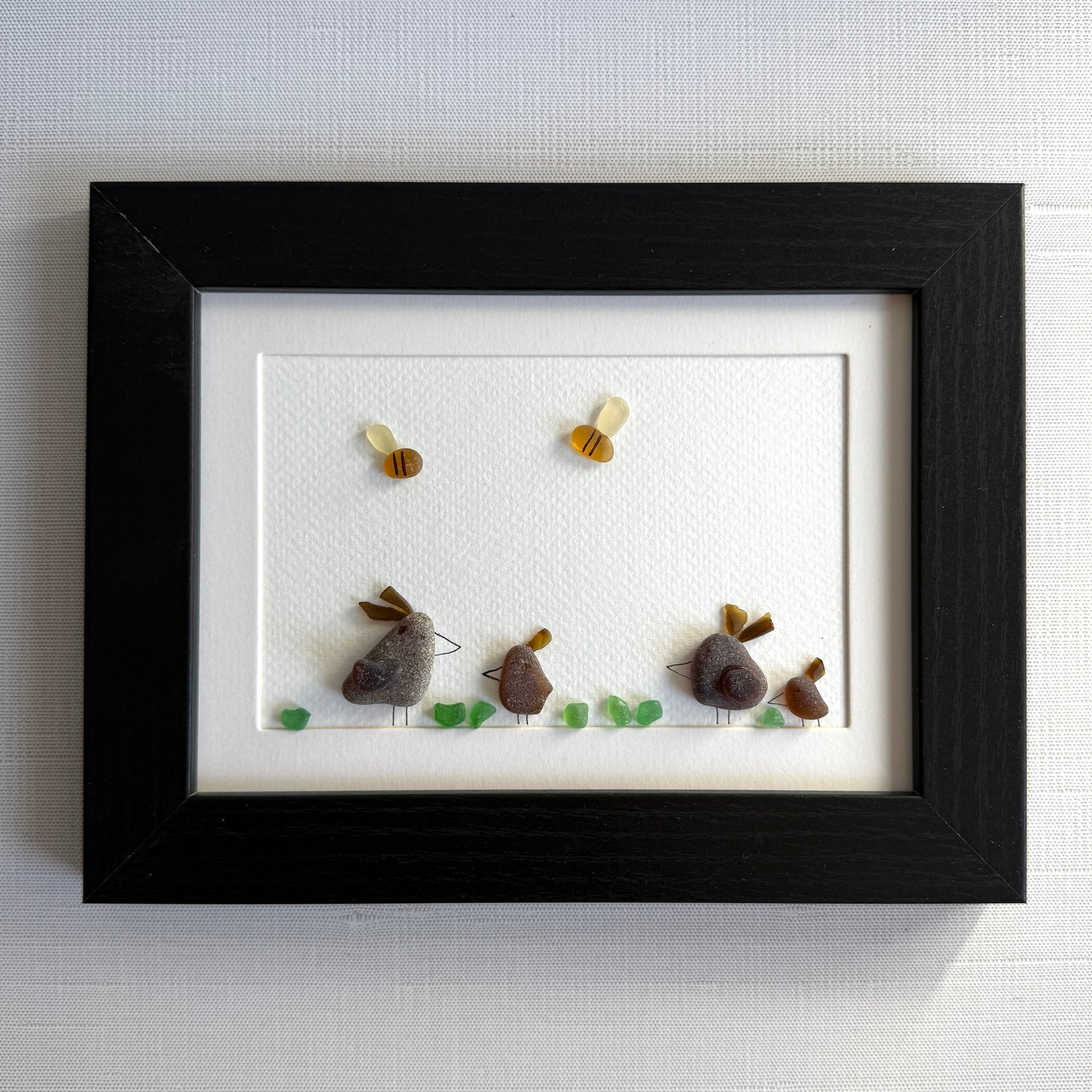 Framed sea glass artwork of hens and chickens on a white background with a black frame.