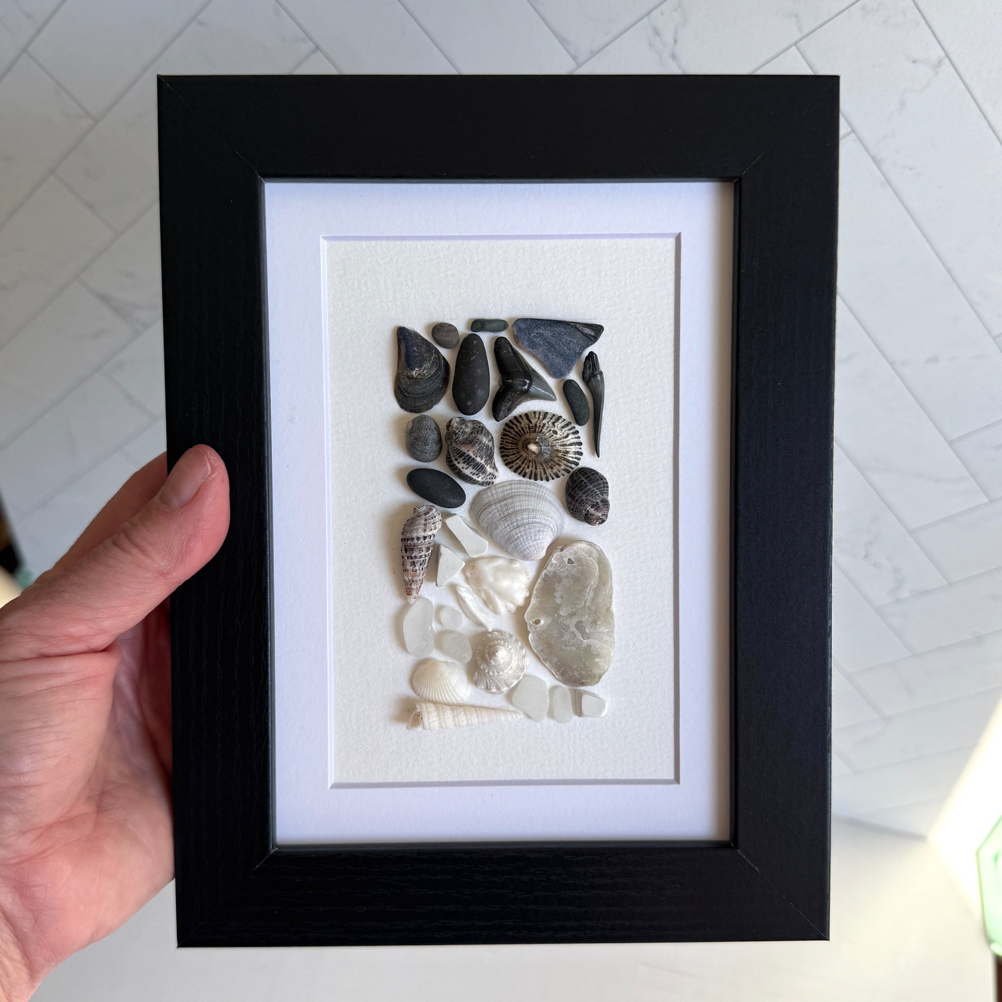 Framed artwork of pebbles, shells and sea glass on a white background
