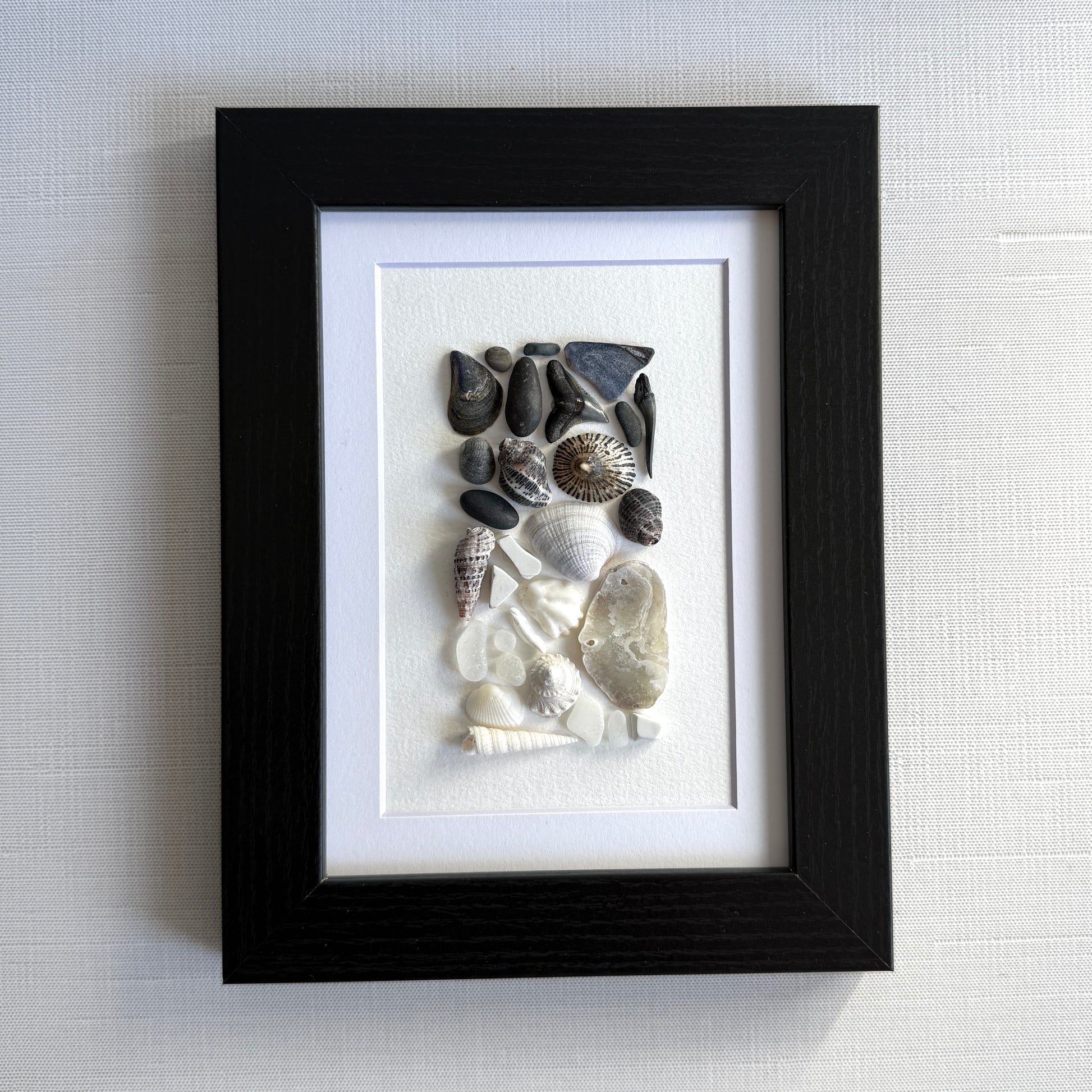 Framed artwork of pebbles, shells and sea glass on a white background